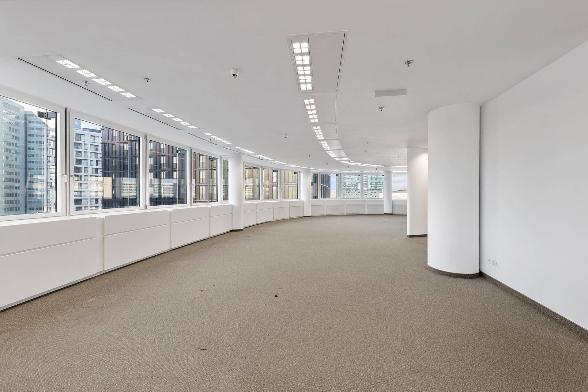 Großer, leerer Büroraum mit geschwungener Fensterfront und Blick auf die Stadt.