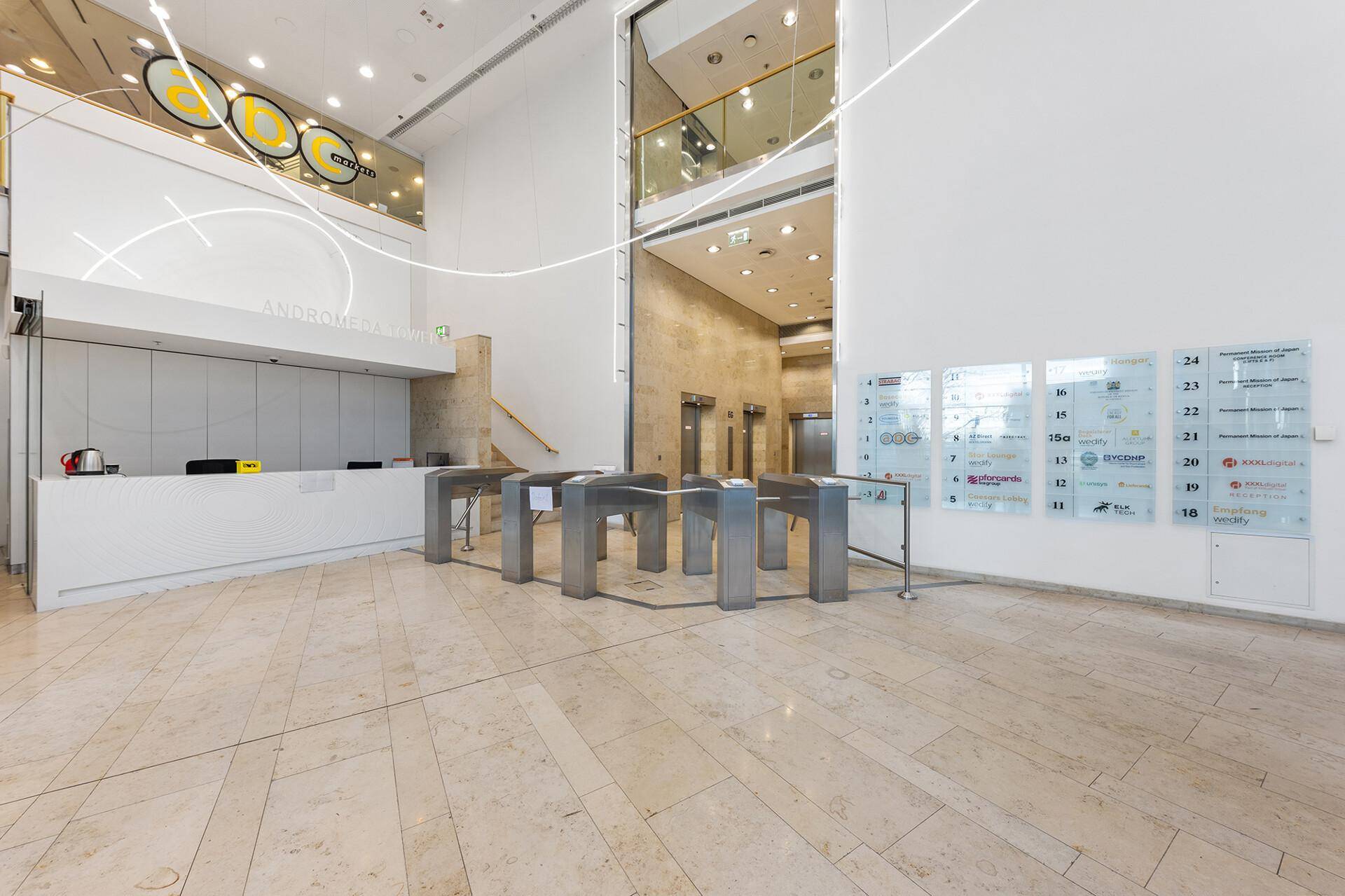 Helle und moderne Lobby mit Rezeption, Zugangskontrolle und Aufzügen im Hintergrund.