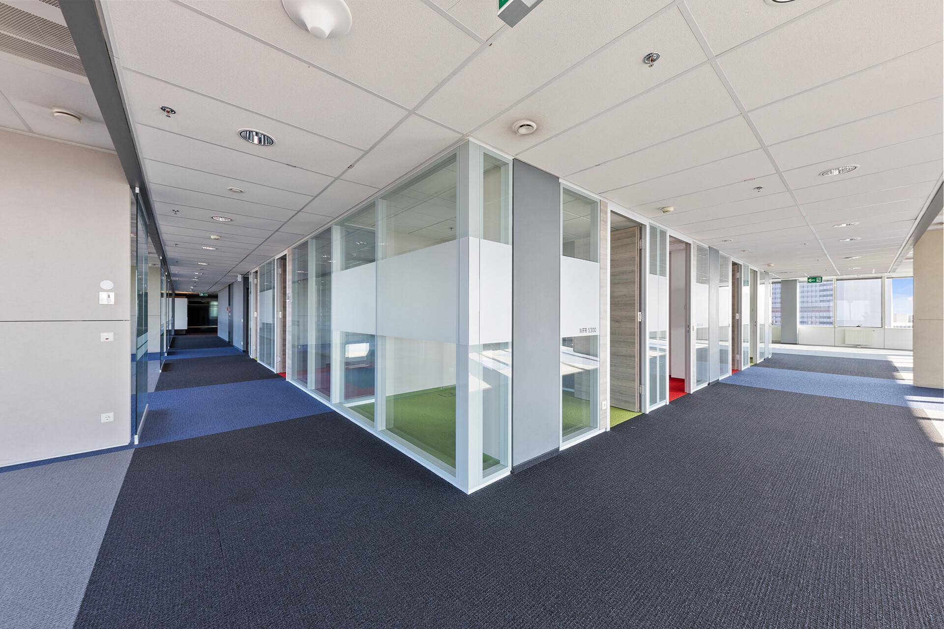 Moderner Büroflur mit Glaswänden, die zu einzelnen Büros führen, und dunklem Teppichboden.