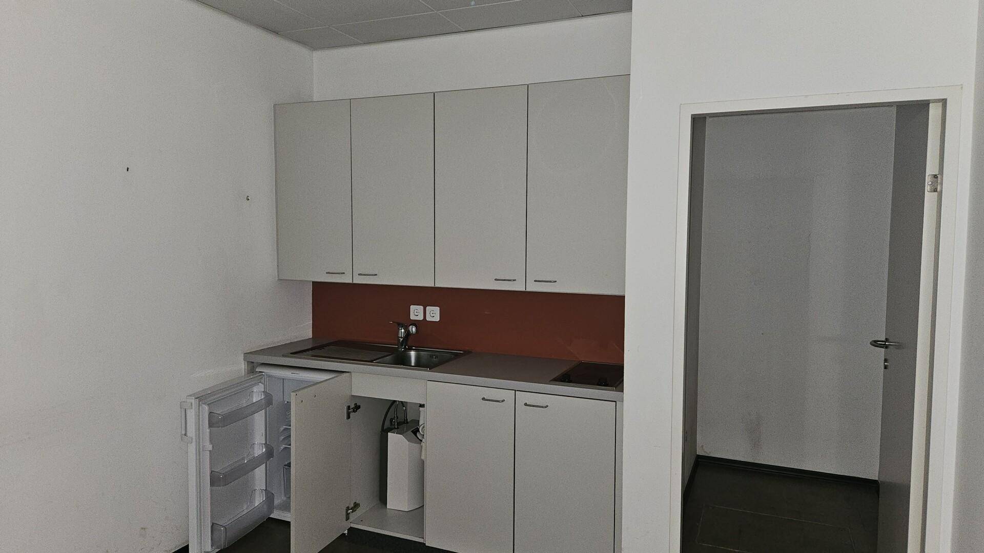 Kleine Einbauküche mit grauen Schränken, Spüle, Kochfeld und einem Kühlschrank.