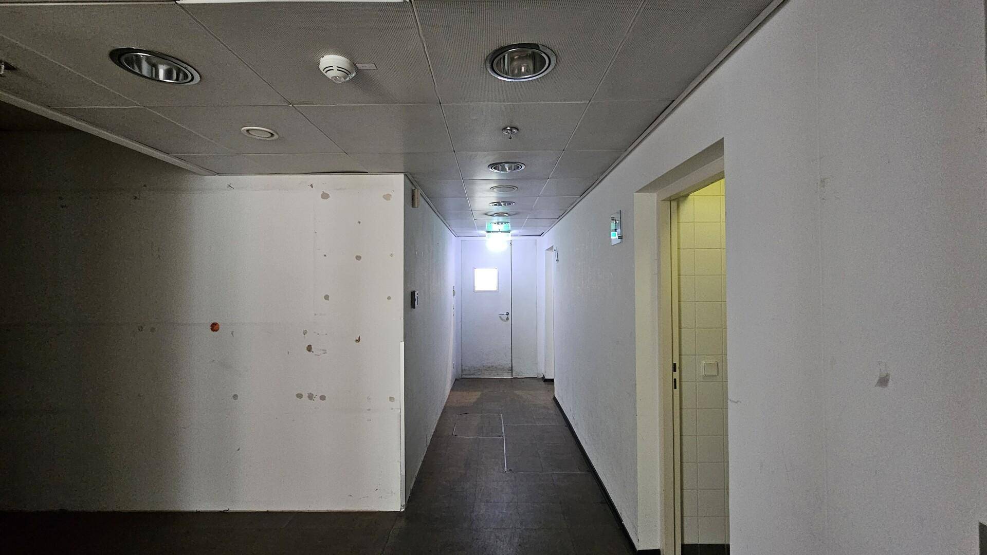 Langer, schlichter Flur mit weißen Wänden, abgehängter Decke und Türen zu weiteren Räumen.