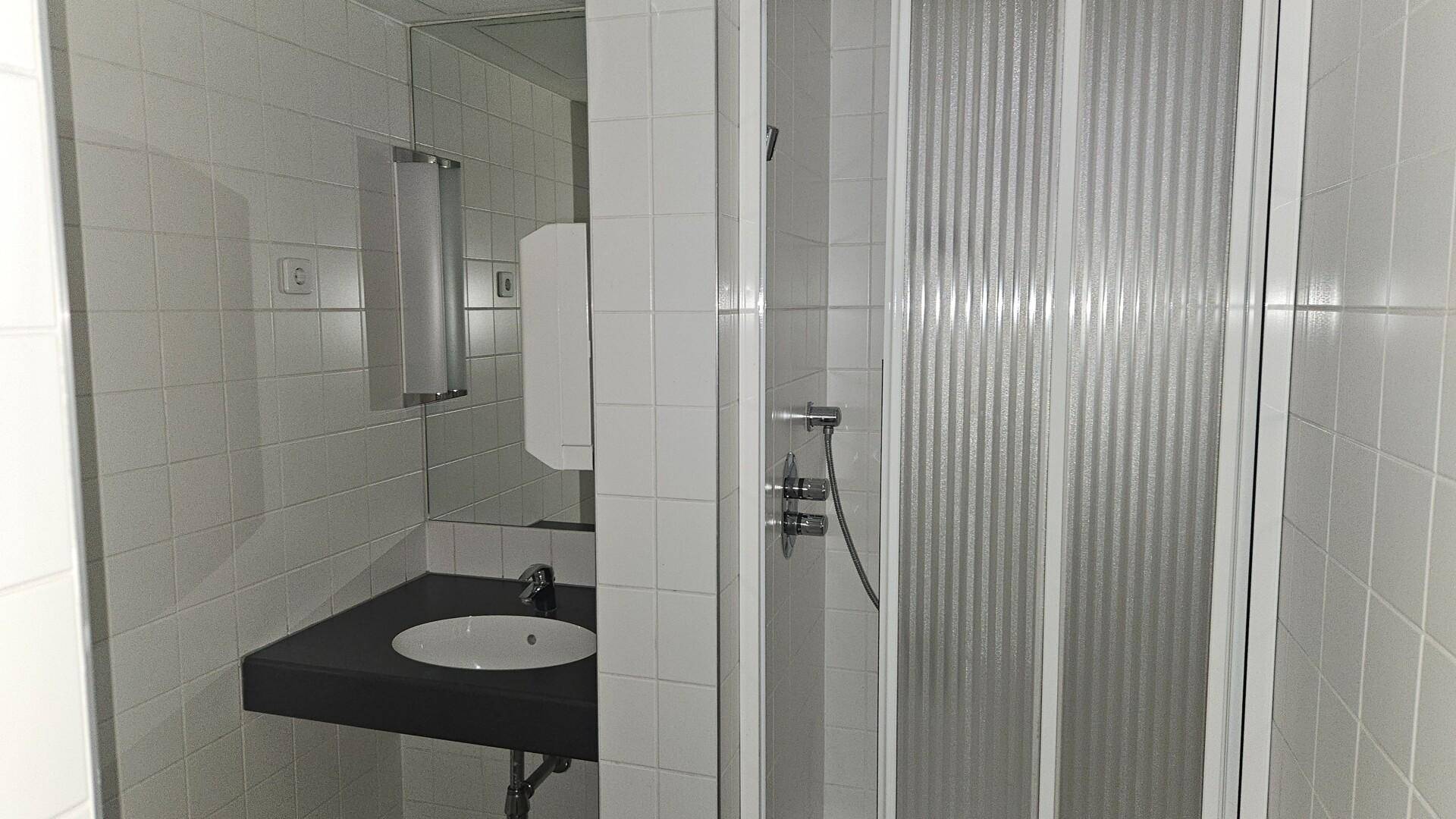 Gefliestes Badezimmer mit Waschbecken, Spiegel und einer Duschkabine mit Falttür.