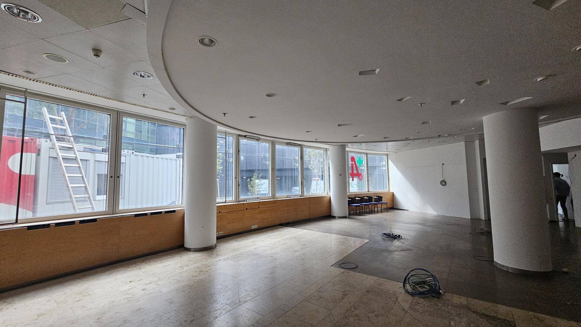 Geräumiger, leerer Büroraum mit großen Fenstern, abgehängter Decke und runden Säulen.