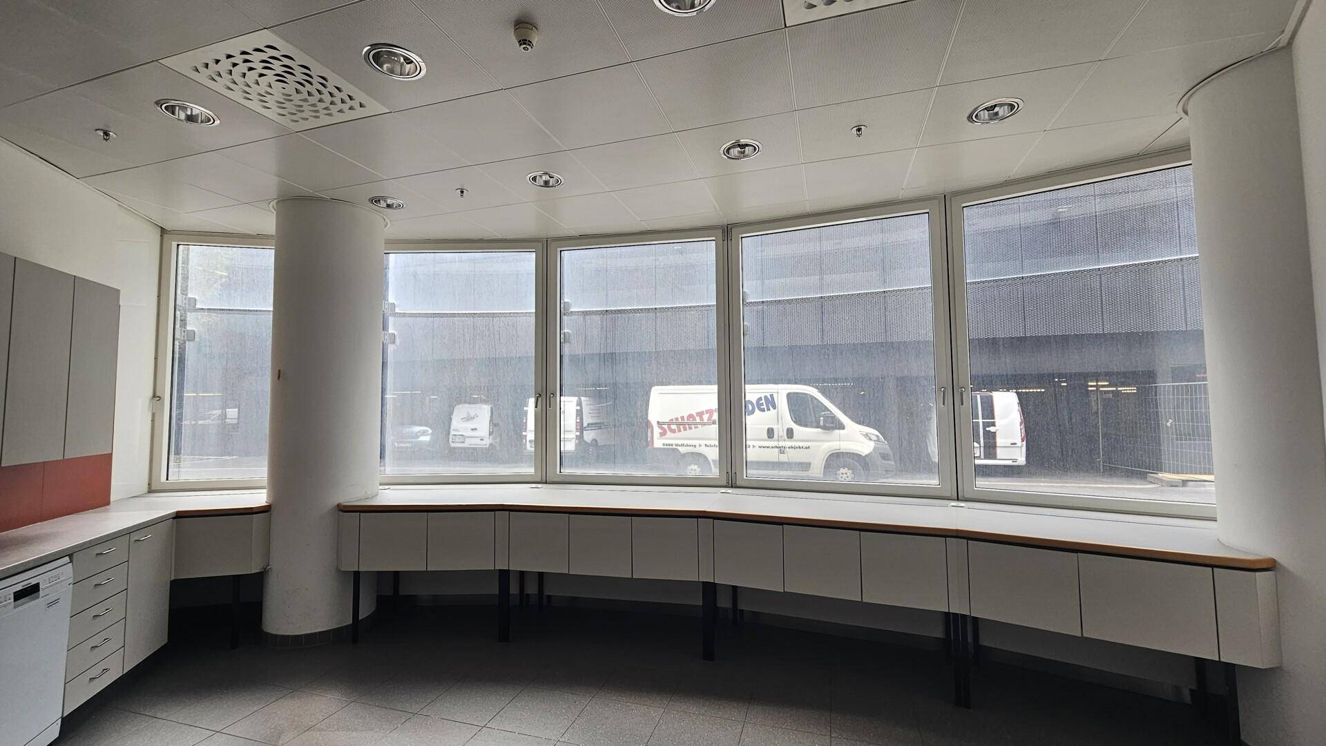 Büroraum mit langer, geschwungener Arbeitsfläche entlang der Fensterfront und abgehängter Decke.