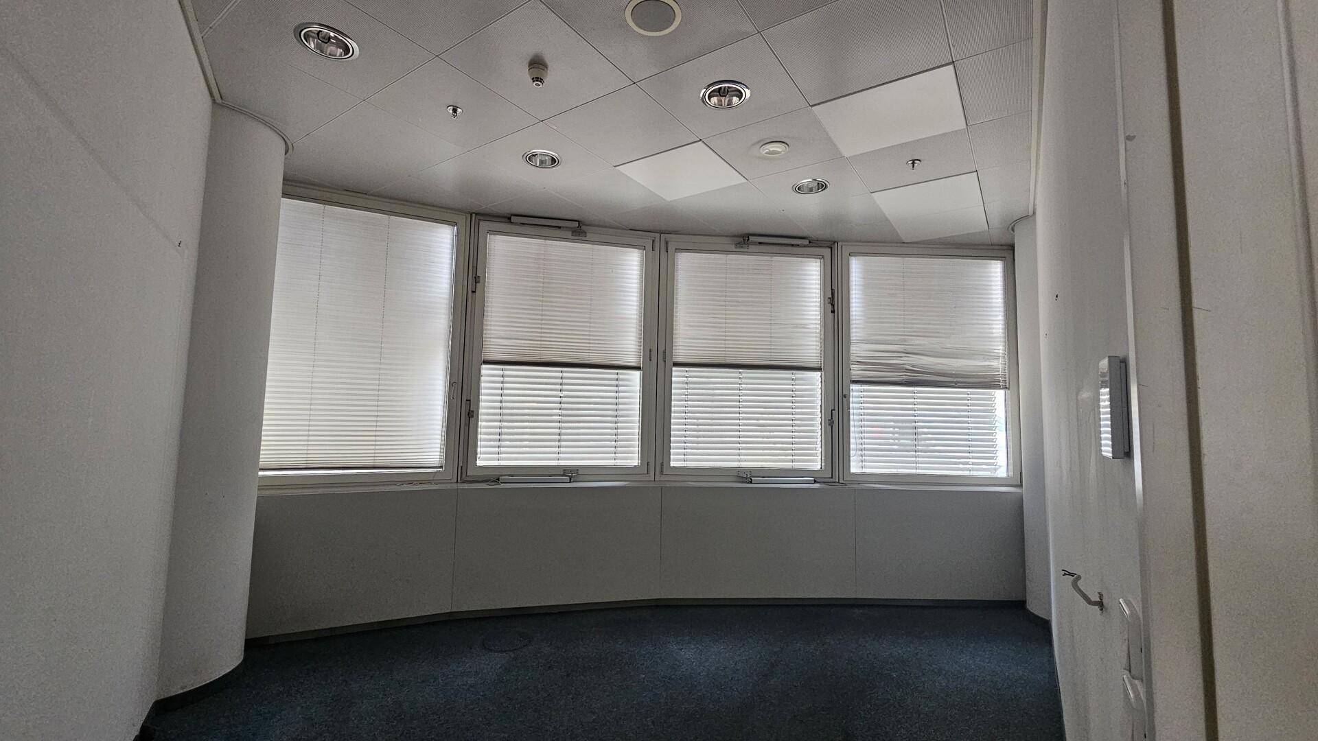 Leeres Büro mit Teppichboden und Fenstern, die mit Jalousien für Privatsphäre ausgestattet sind.