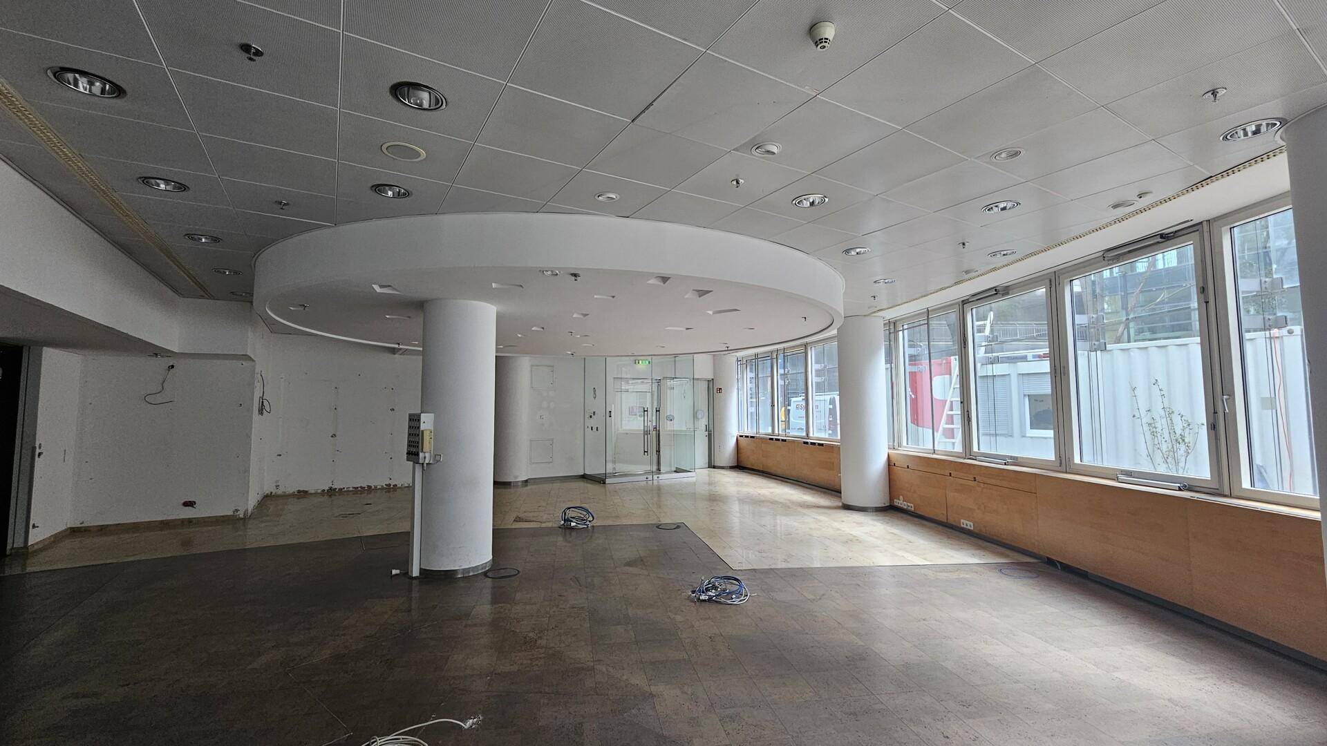 Weitläufiger Bürobereich mit heller Fliesenboden, runden Säulen und viel Tageslicht durch die Fensterfront.