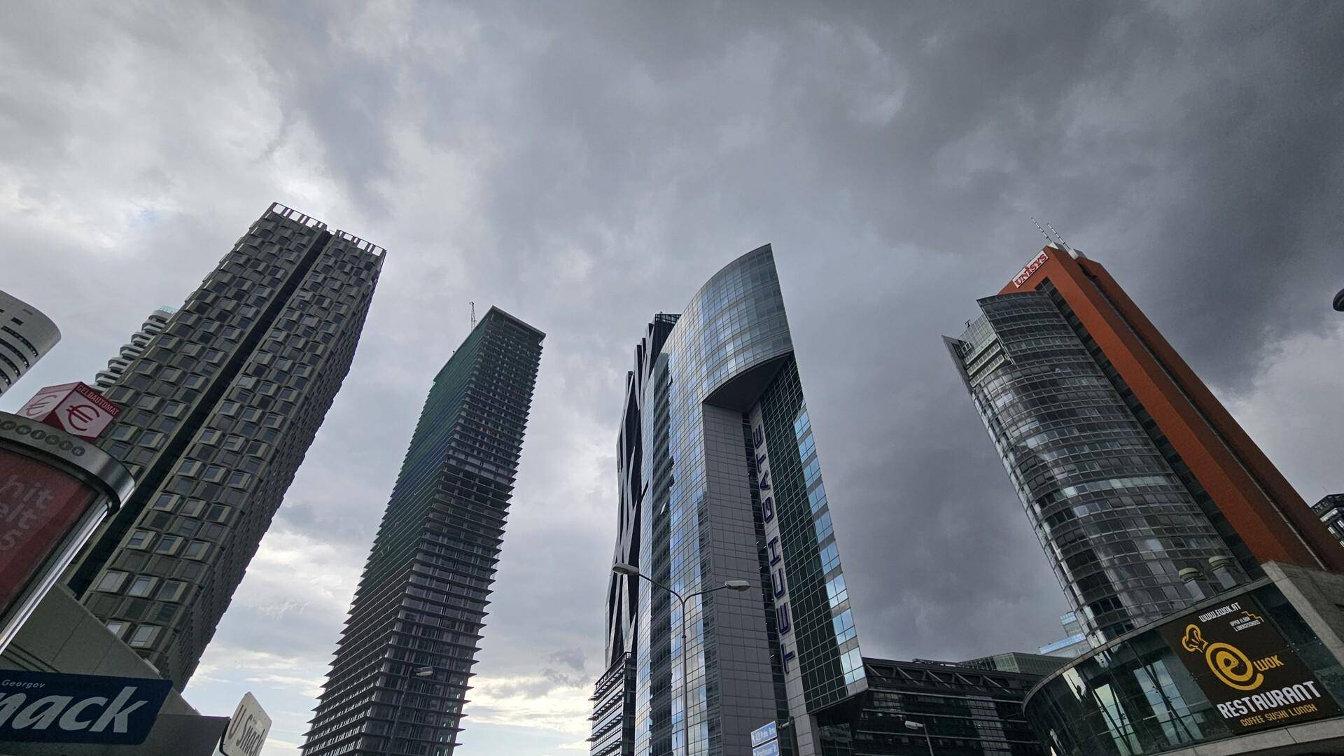 Mehrere moderne Hochhäuser mit Glas- und Metallfassaden ragen unter einem bewölkten Himmel auf.