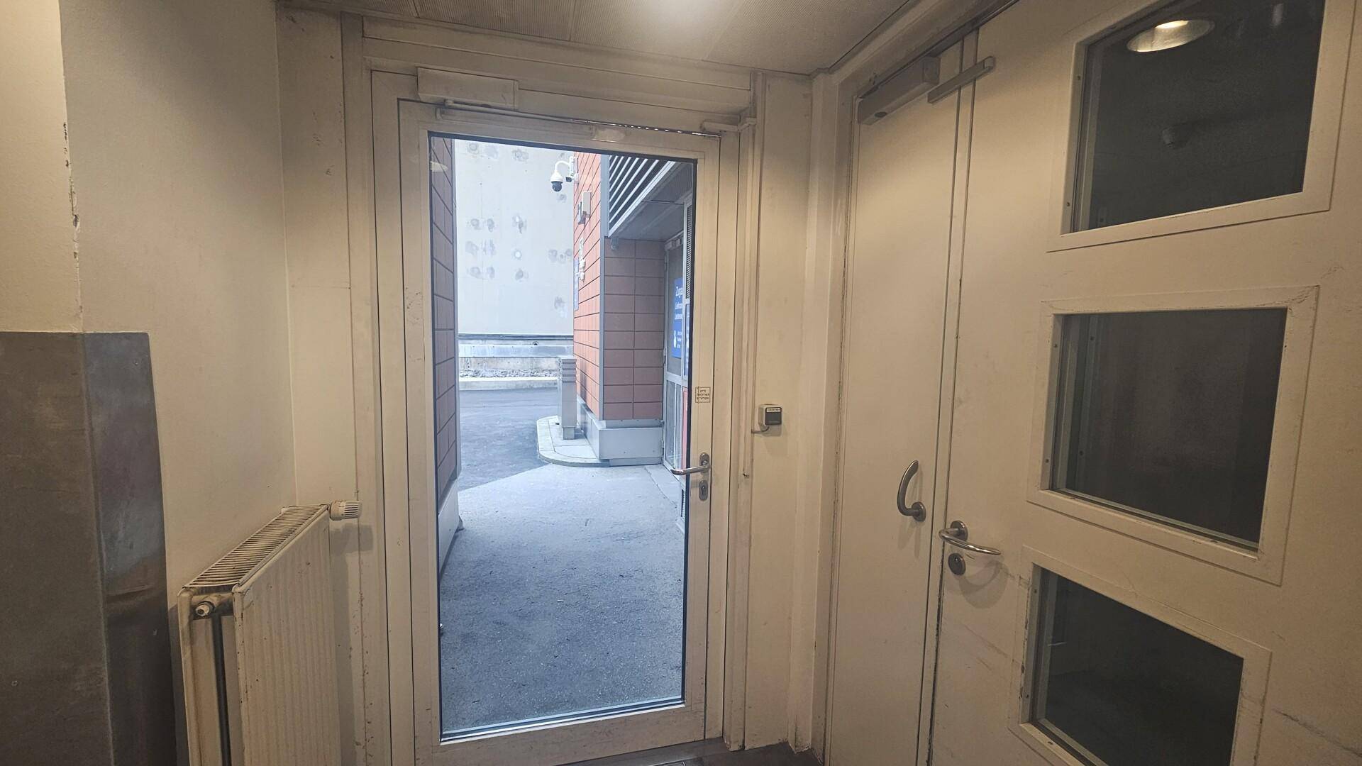 Eingangsbereich mit Glastür, die zu einem Außenbereich führt, und einem Heizkörper an der Wand.