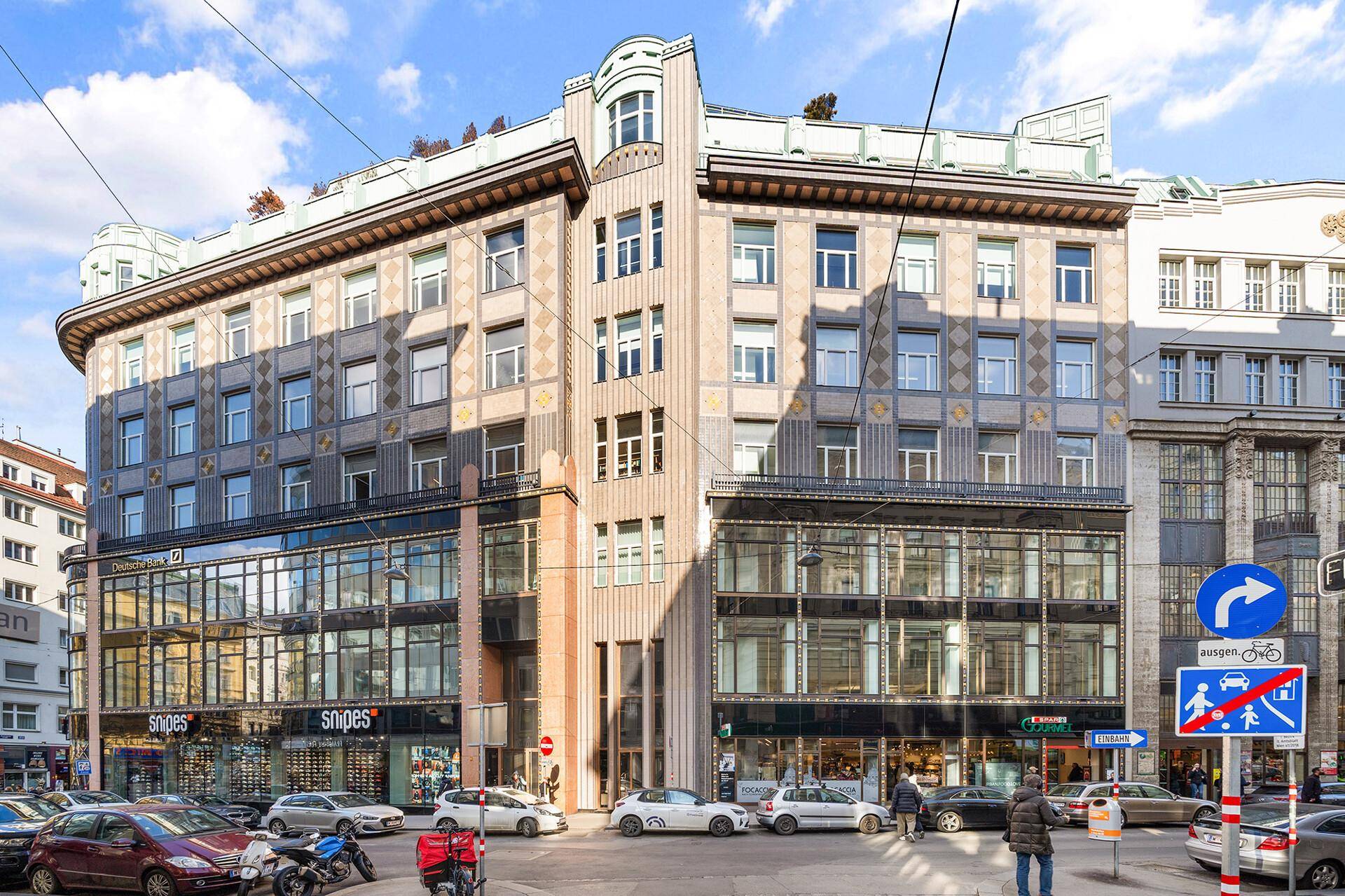 Historisches Gebäude mit markanter Architektur und Geschäften im Erdgeschoss an einer belebten Straße.