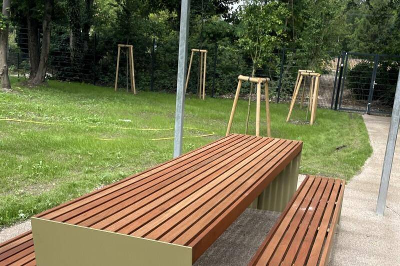 Detailansicht des Holztisches mit Bänken unter einer Pergola im grünen Gemeinschaftsgarten.