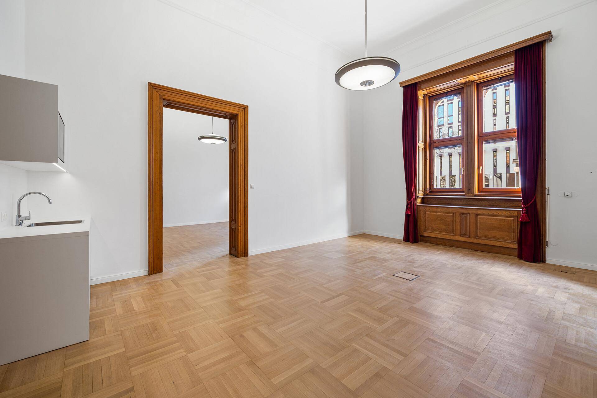 Geräumiger Raum mit Fischgrätparkett, hohen Decken und einer kleinen Küchenzeile, ideal als Büro.