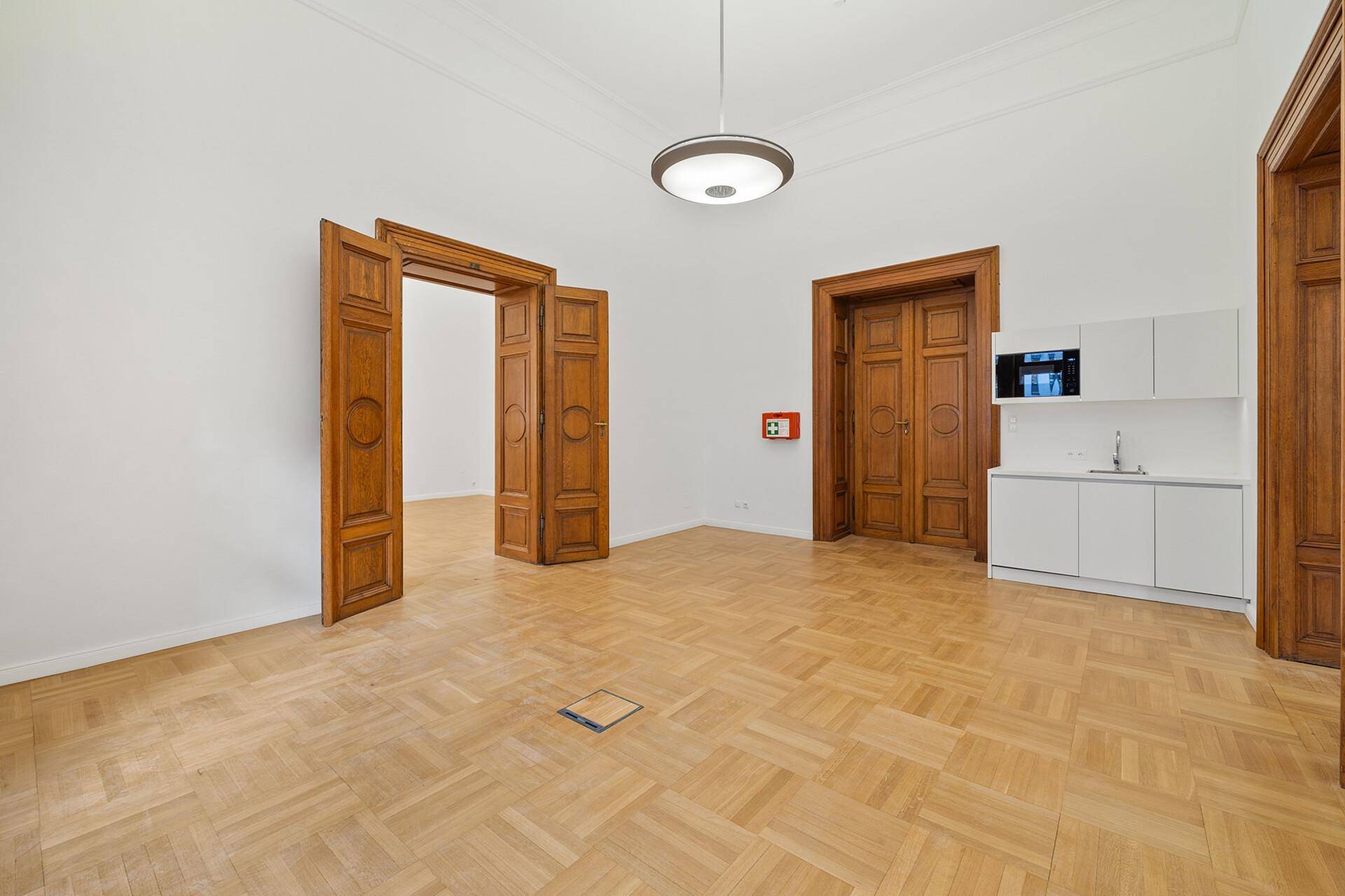 Heller Raum mit Fischgrätparkett, hohen Decken und einer praktischen Küchenzeile, verbunden durch Holztüren.