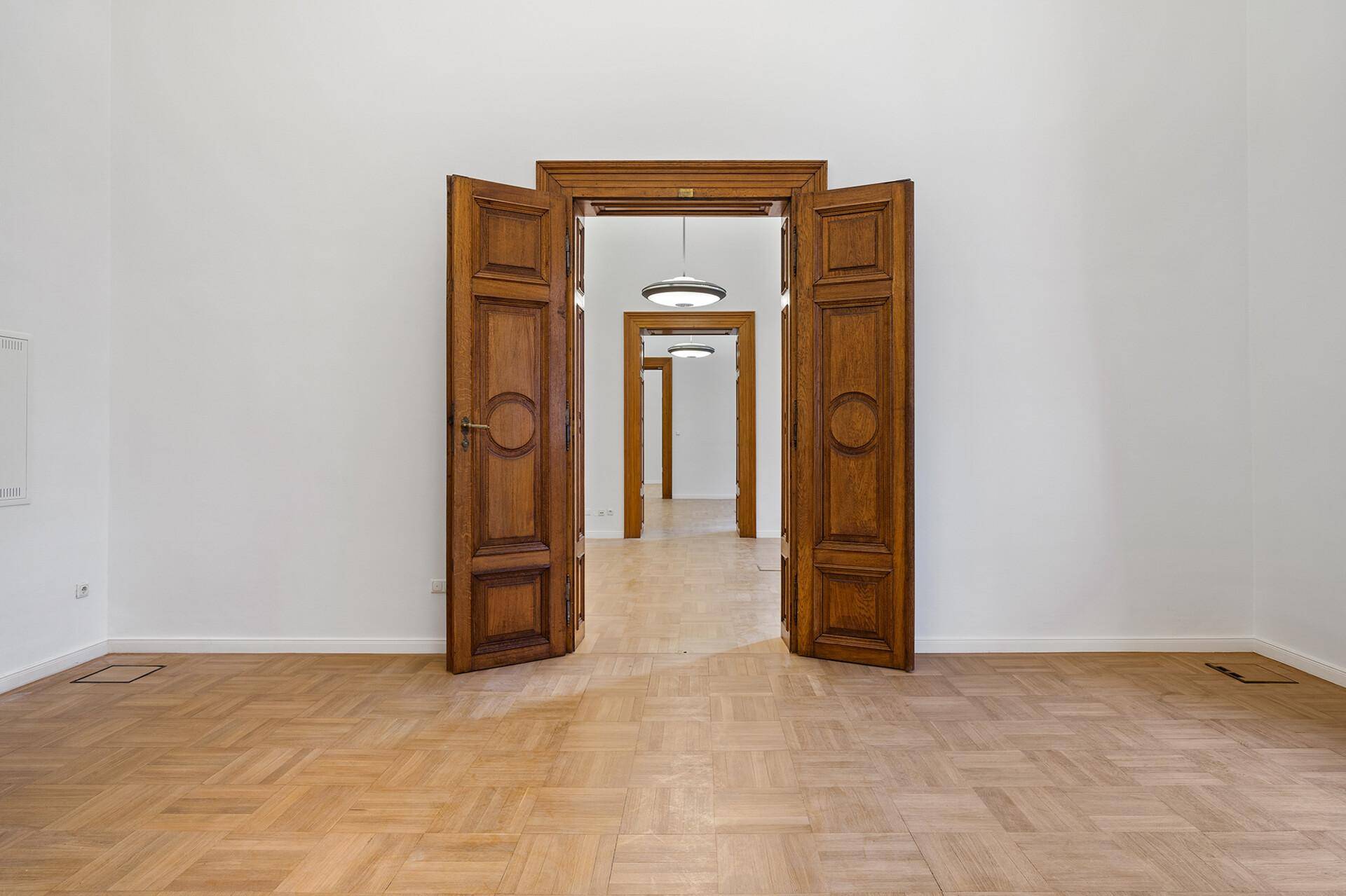 Langer Flur mit Fischgrätparkett und einer Reihe von eleganten Holztüren, die zu weiteren Räumen führen.