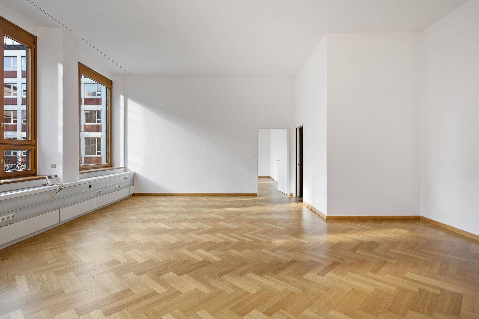 Heller Büroraum mit Fischgrätparkett und großen Holzfenstern, die viel Tageslicht hereinlassen.