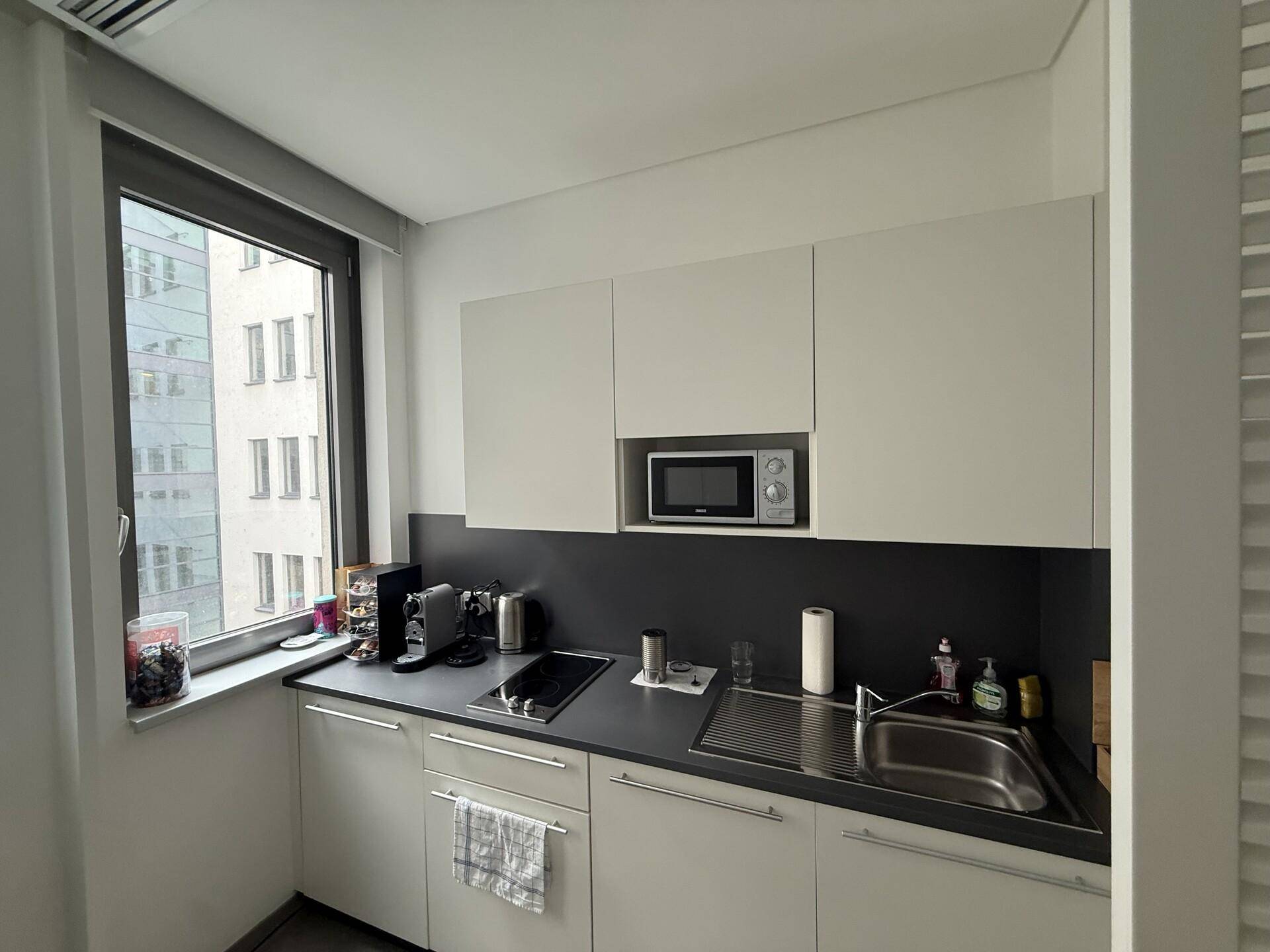 Kompakte Küchenzeile mit Mikrowelle, Induktionskochfeld und Spüle unter einem Fenster.