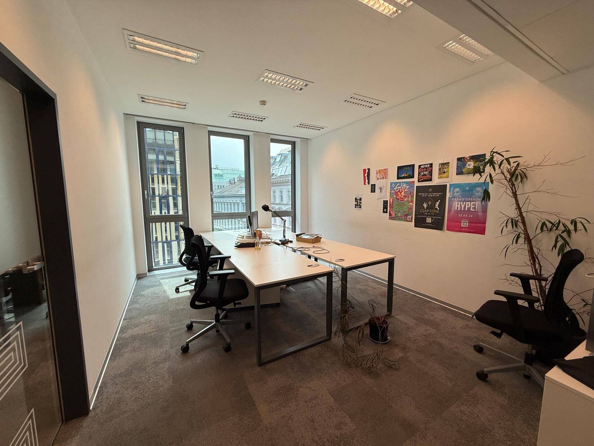 Modernes Büro mit zwei Arbeitsplätzen, Teppichboden und Blick auf die Stadt durch große Fenster.