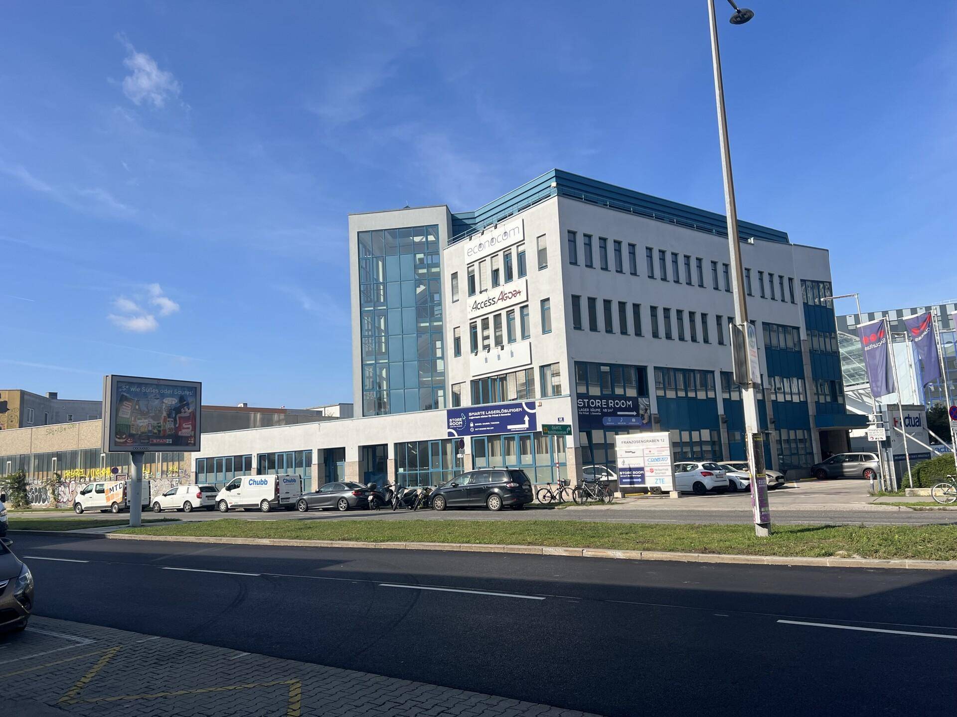 Modernes Bürogebäude mit blauer Fassade und vielen Fenstern an einer belebten Straße.