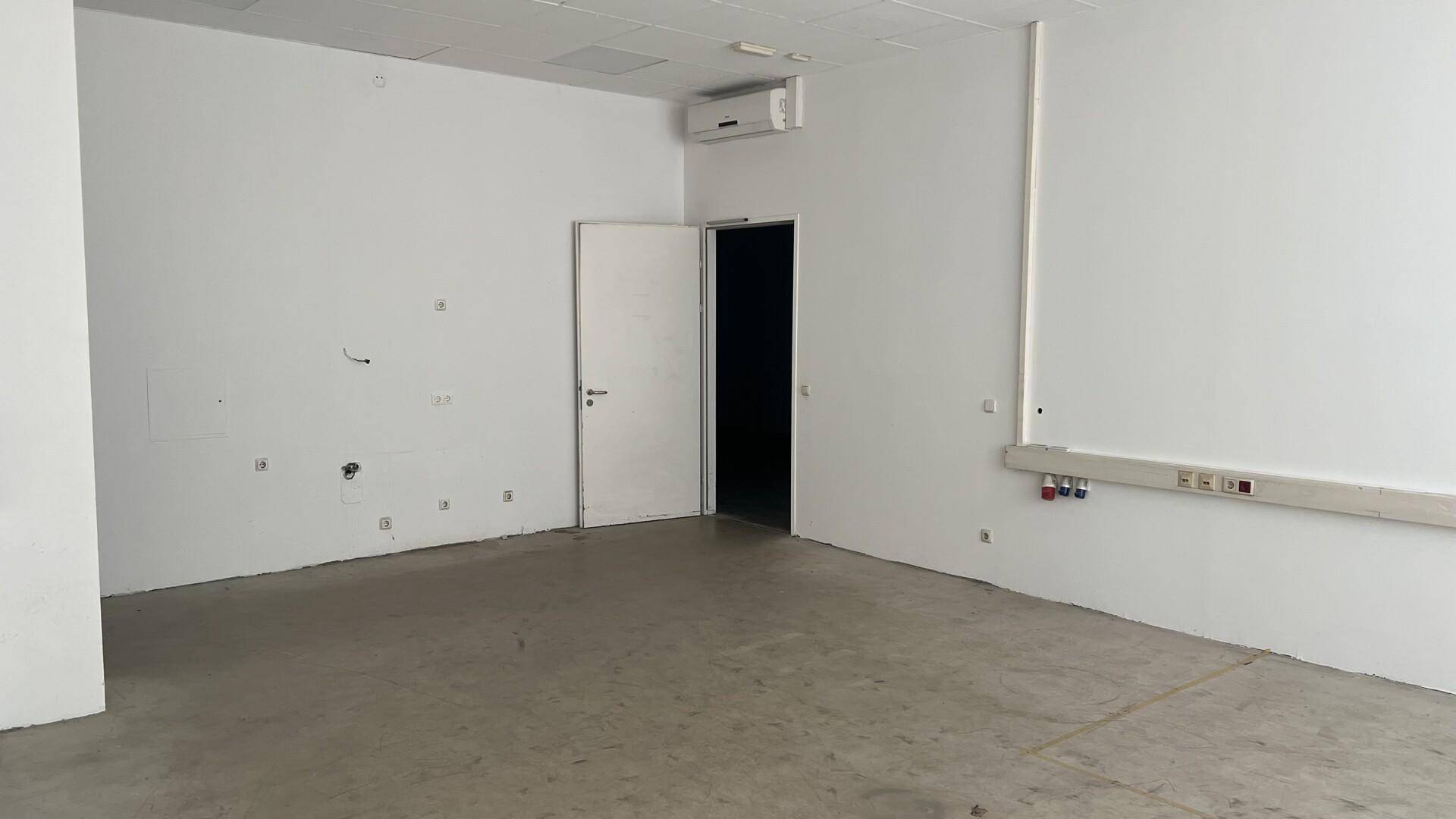 Heller, leerer Büroraum mit Klimaanlage, weißen Wänden und Betonboden.