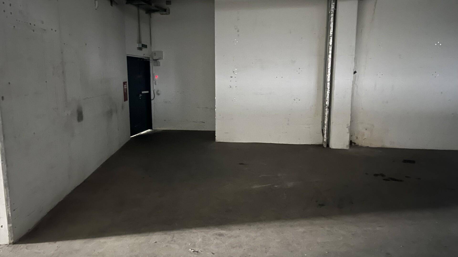 Kleinerer, leerer Raum mit Betonboden und einer dunklen Tür, ideal als Abstellraum.