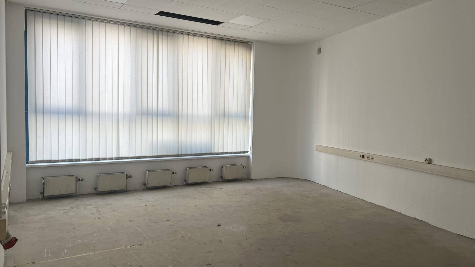 Geräumiger Büroraum mit großer Fensterfront, Jalousien und Heizkörpern unter dem Fenster.