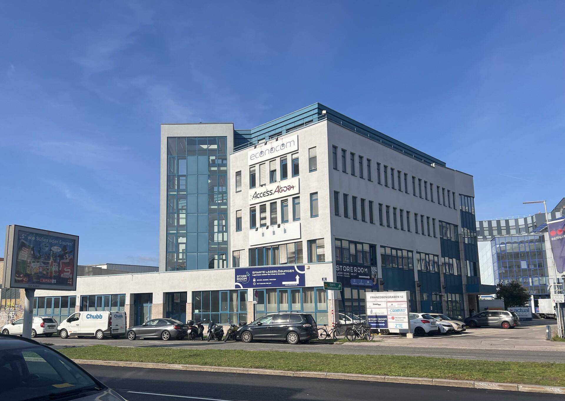 Modernes Bürogebäude mit Glasfassade und blauen Akzenten, umgeben von Parkplätzen.