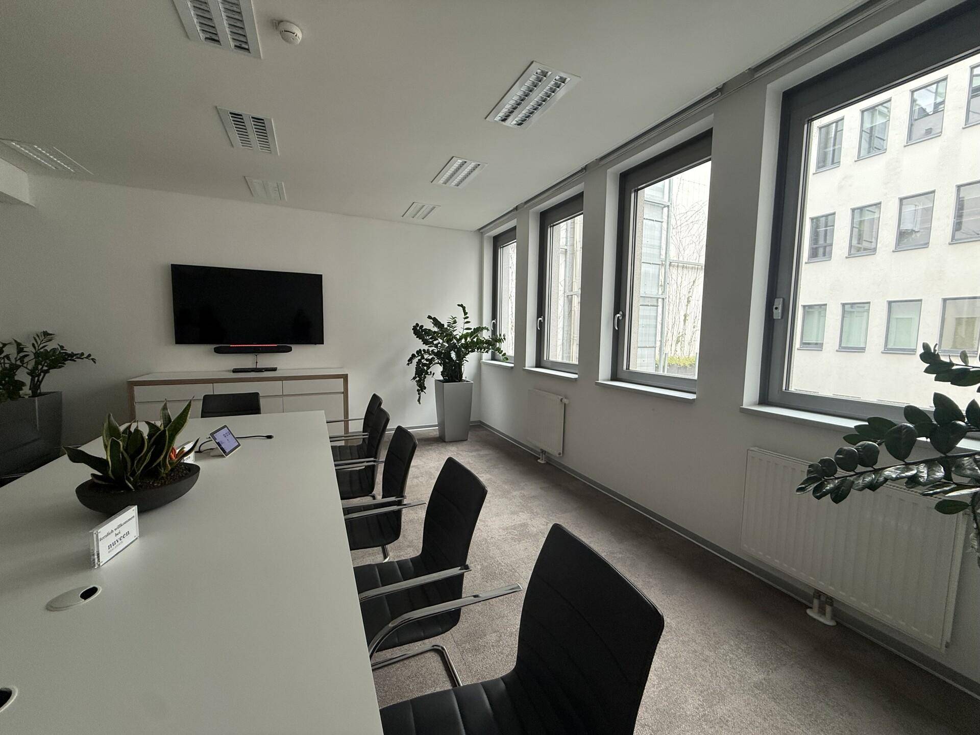 Heller Konferenzraum mit großem Tisch, Wandfernseher und Blick auf die umliegenden Gebäude.