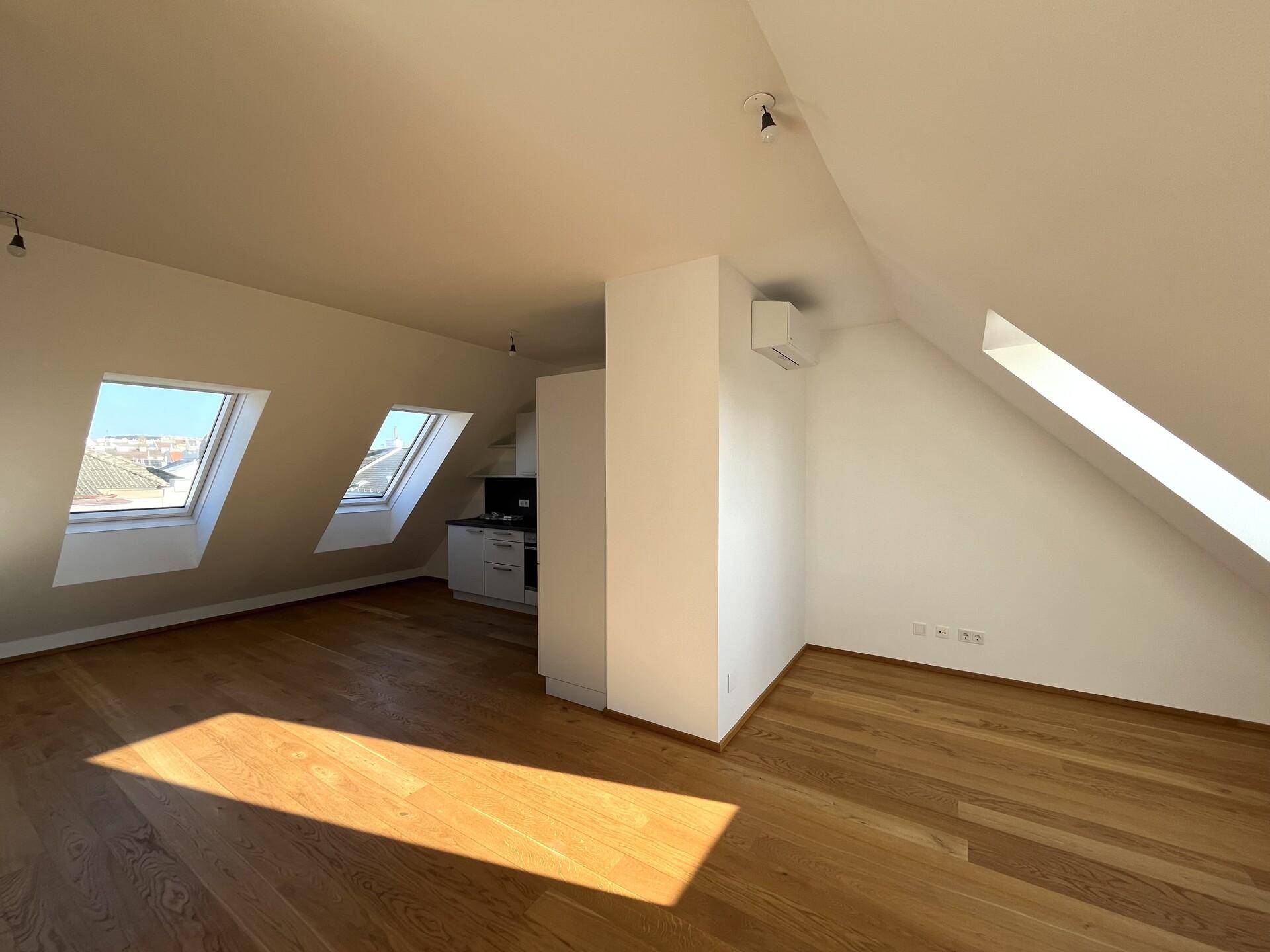 Lichtdurchfluteter Wohnbereich im Dachgeschoss mit Holzboden, Klimaanlage und schrägen Wänden mit Dachfenstern.