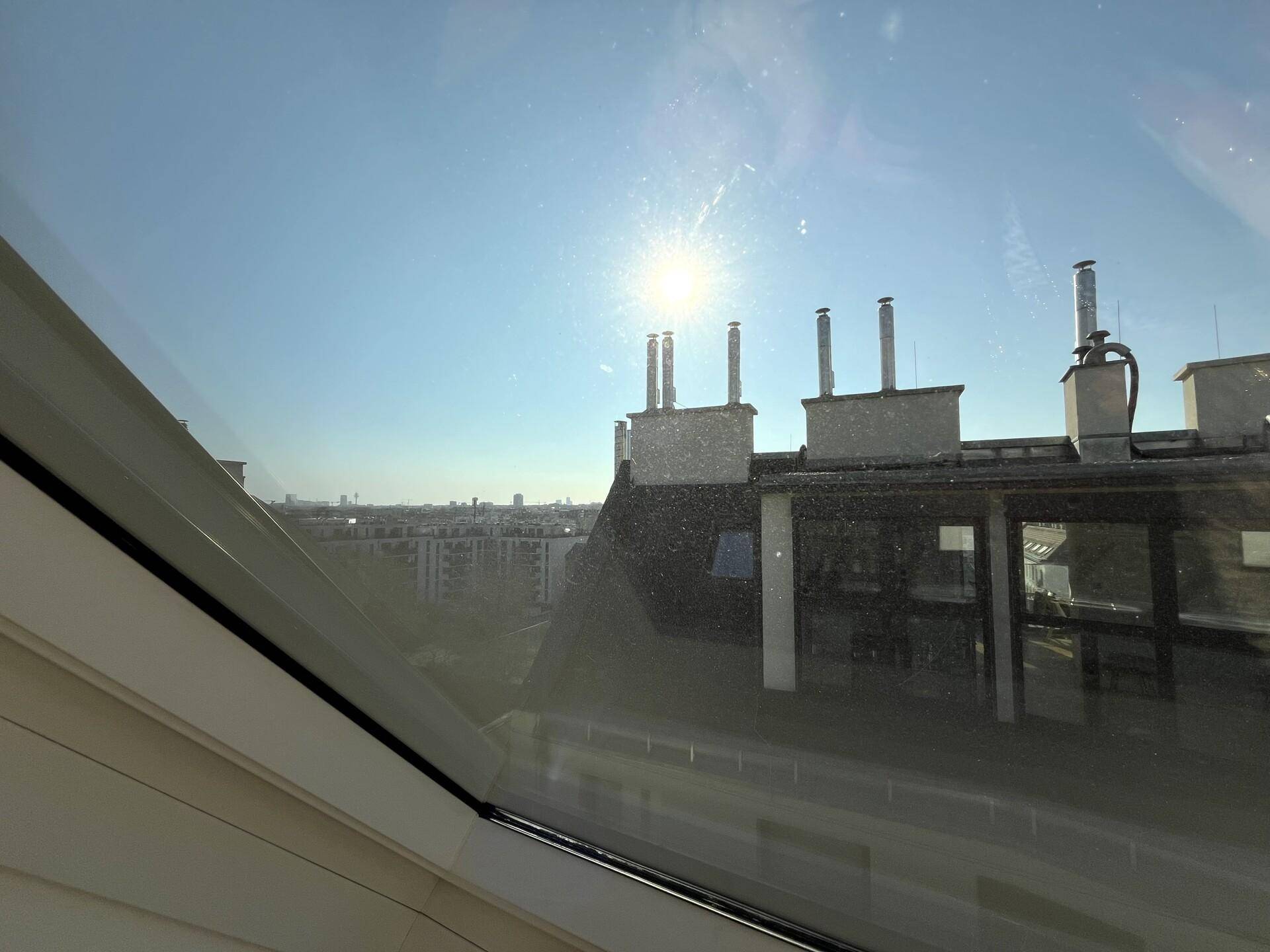 Sonniger Ausblick aus einem Dachfenster auf die umliegenden Dächer und Schornsteine der Stadt.