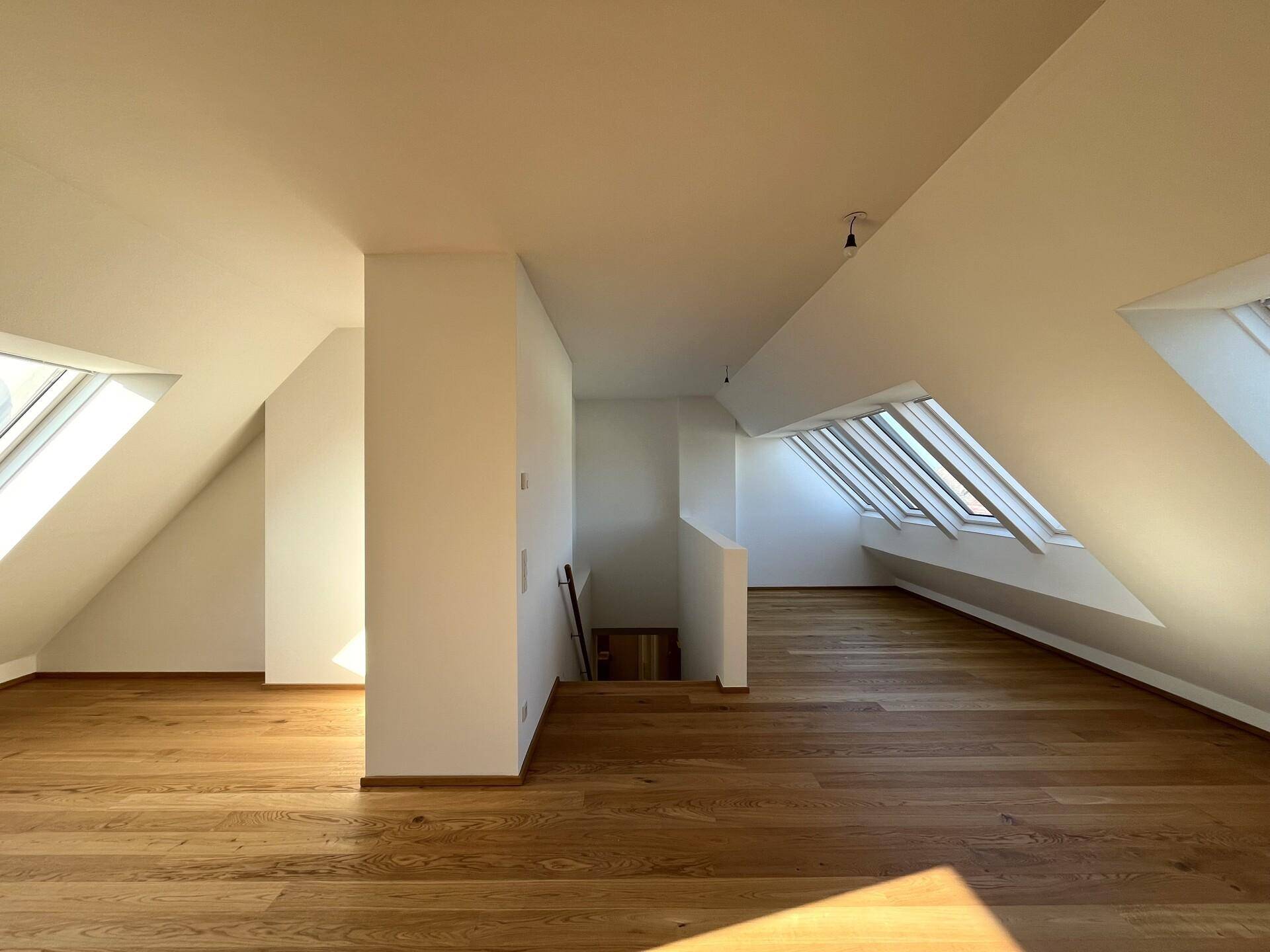Heller Dachgeschoss-Wohnbereich mit Holzboden, schrägen Decken und Dachfenstern, die den Raum mit Licht füllen.