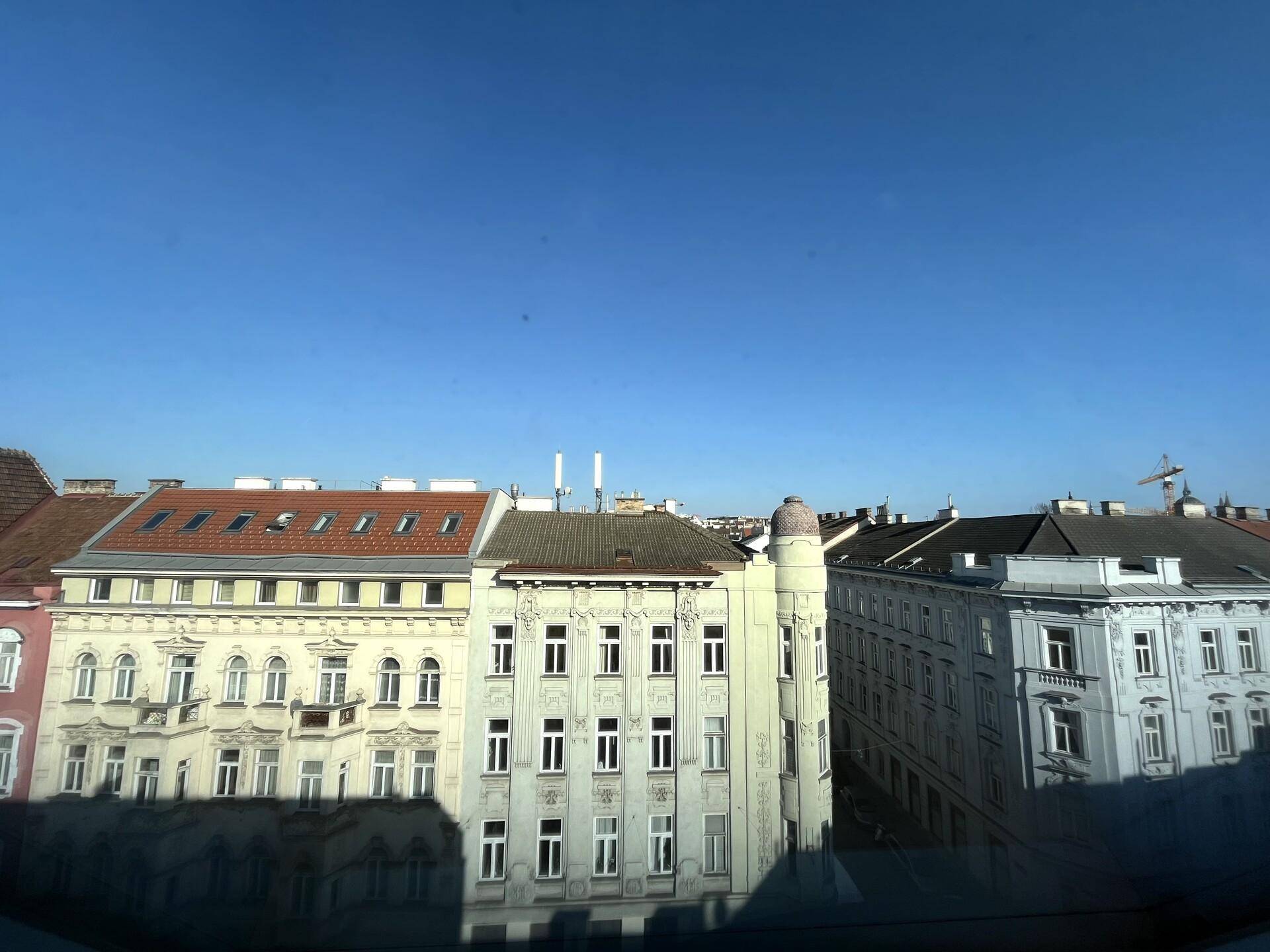 Blick aus dem Fenster auf die historischen Fassaden der gegenüberliegenden Gebäude unter blauem Himmel.