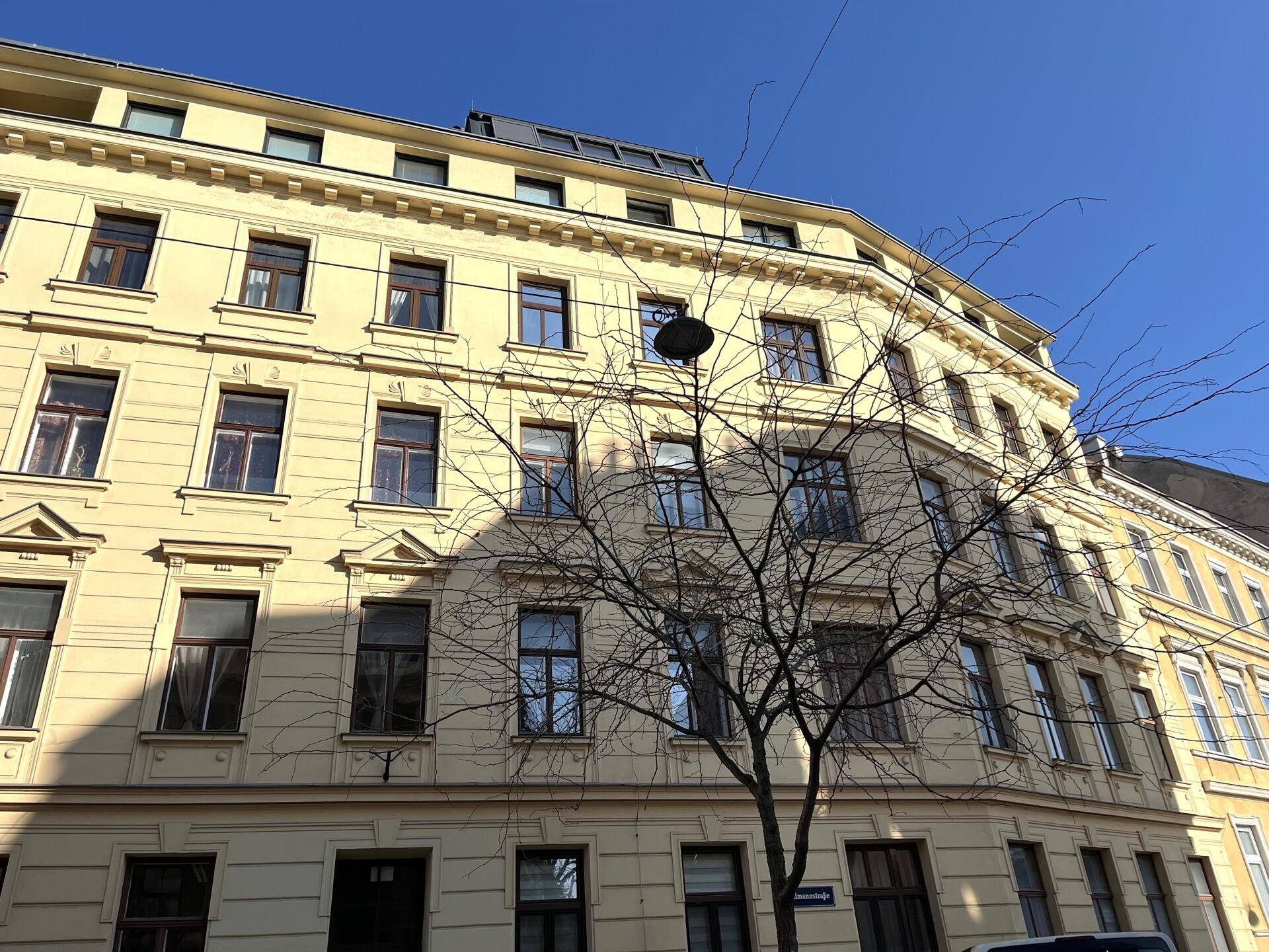 Historische Fassade eines Altbaus mit gelbem Anstrich und zahlreichen Fenstern unter blauem Himmel.