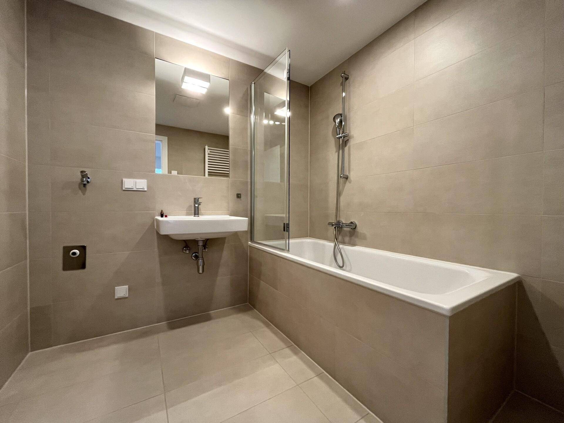 Modernes Badezimmer mit beigefarbenen Fliesen, einer Badewanne mit Duschwand und einem einzelnen Waschbecken.