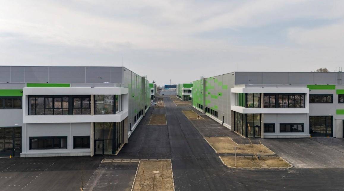 Ansicht von zwei modernen Industriegebäuden mit großen Fensterfronten und breiter Zufahrtsstraße für Fahrzeuge.