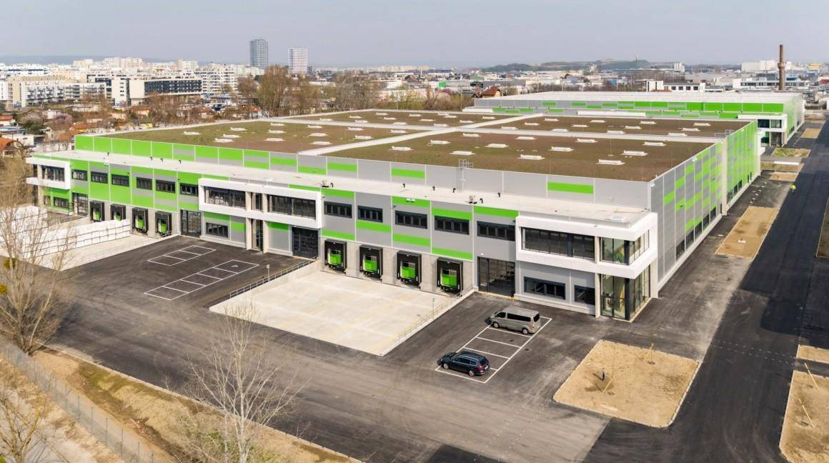 Außenansicht einer modernen Industriehalle mit Laderampen und großzügigen Parkflächen unter klarem Himmel.