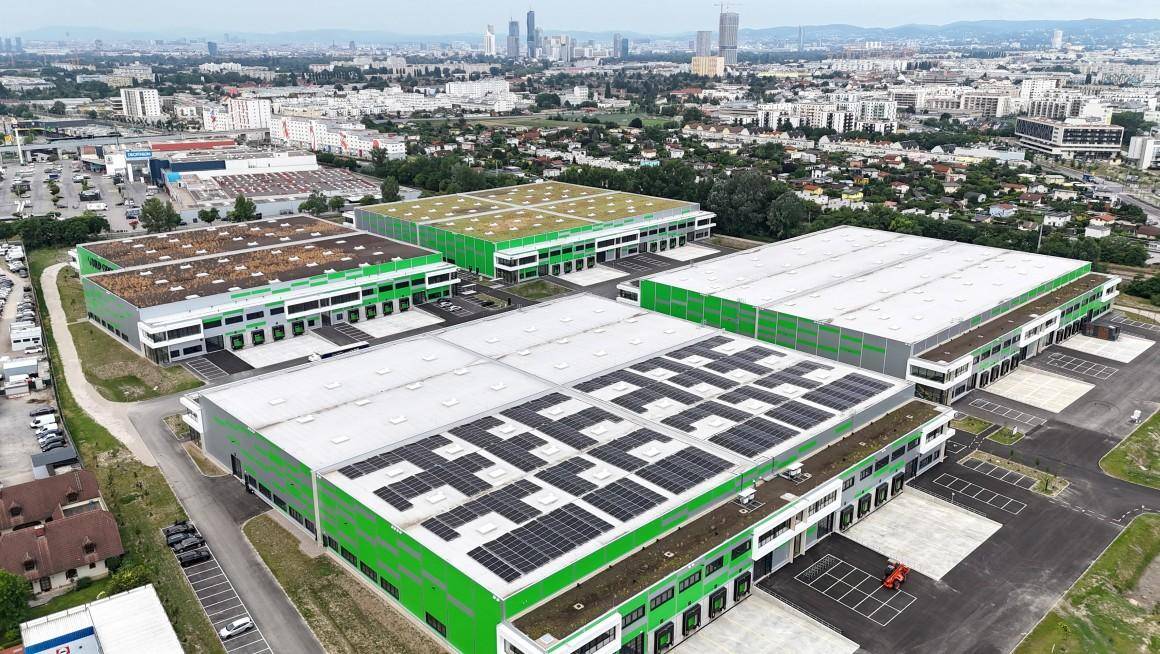 Luftbild einer modernen Industrieanlage mit mehreren Hallen und Photovoltaikanlagen auf den Dächern.