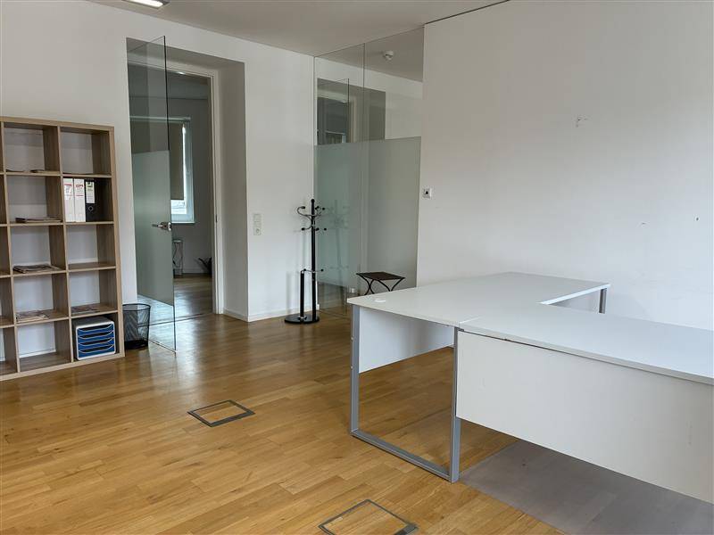 Modernes Büro mit Glaswänden, Holzfußboden und einem leeren Schreibtischbereich.
