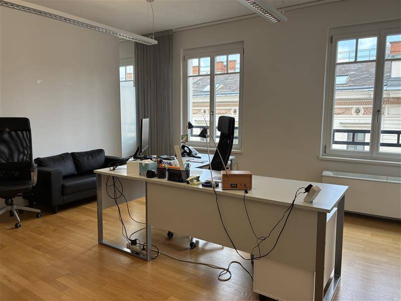 Helles Büro mit Schreibtisch, Bürostuhl, Sofa und Blick auf die umliegenden Gebäude.