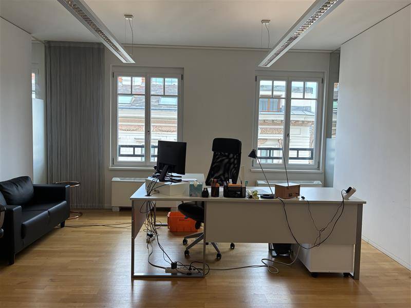 Geräumiges Büro mit Schreibtisch, Bürostuhl, Sofa und Blick auf die umliegenden Gebäude.