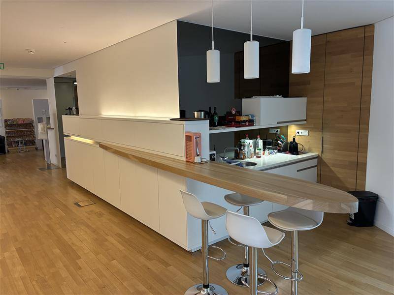 Moderne Küchenzeile mit Holztheke, weißen Schränken und Barhockern in einem offenen Bereich.