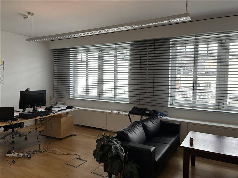 Büro mit Jalousien an den Fenstern, Holzfußboden und einem Sofa im Vordergrund.