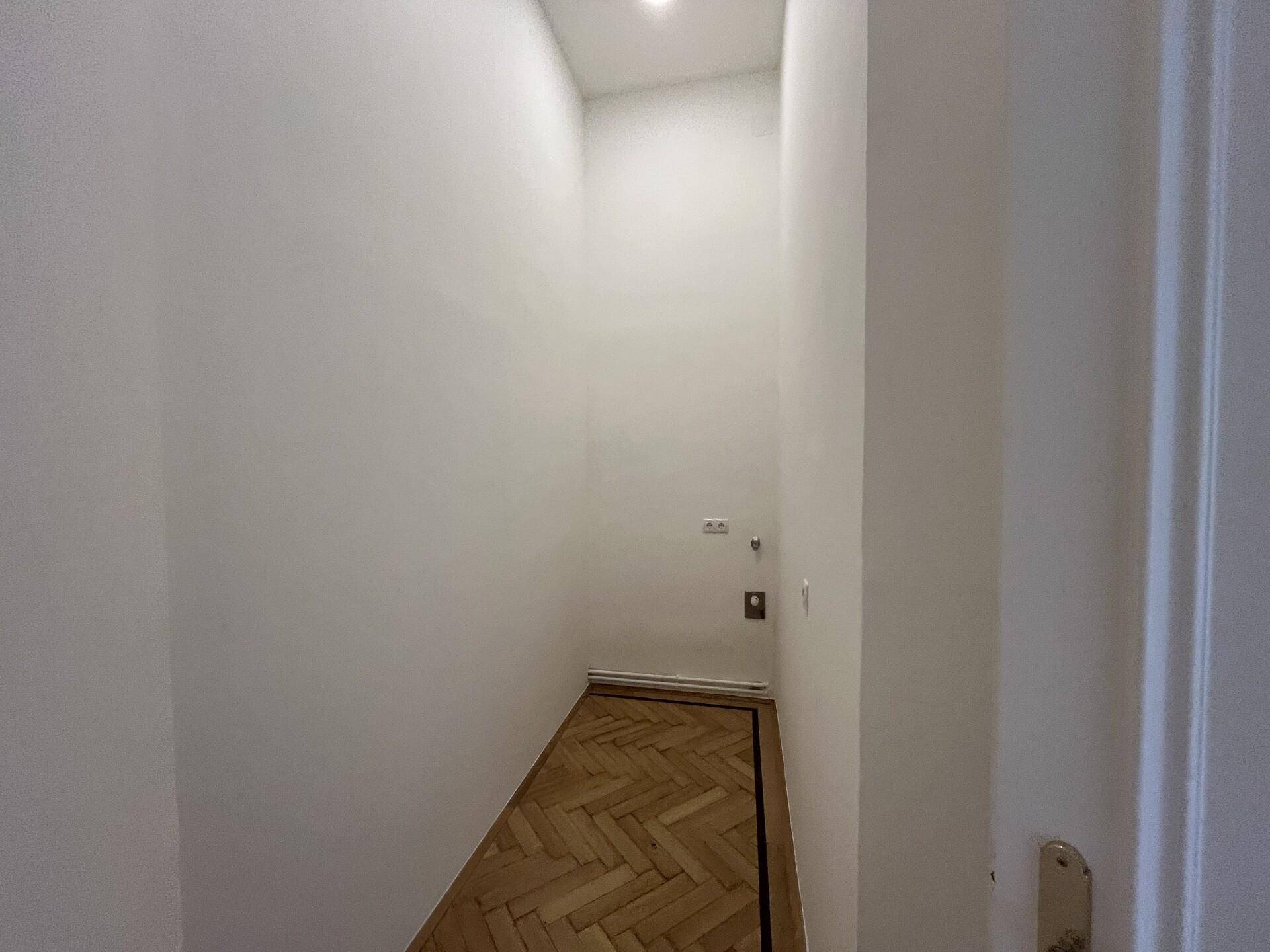 Schmaler, heller Flur mit Fischgrätparkett und weißen Wänden, der zu weiteren Räumen führt.