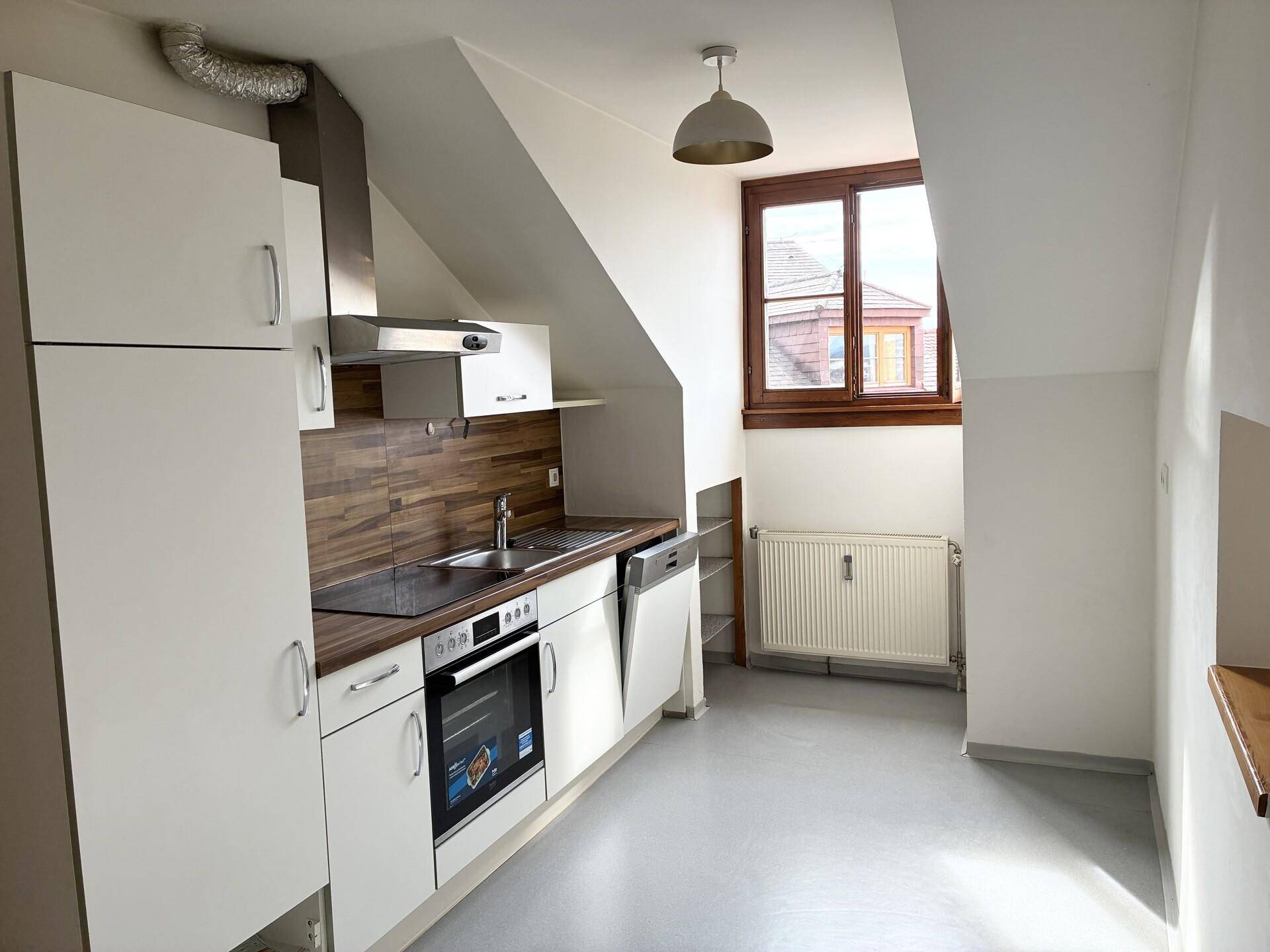 Moderne Küche im Dachgeschoss mit weißen Schränken, Holzakzenten und Dachschräge.