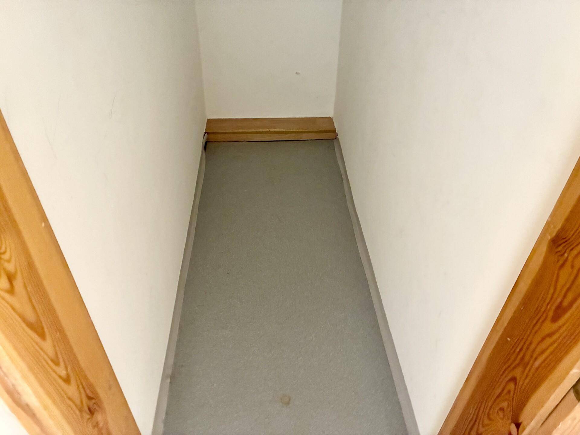 Schmaler Abstellraum mit hellem Boden und sichtbaren Holzkonstruktionselementen.