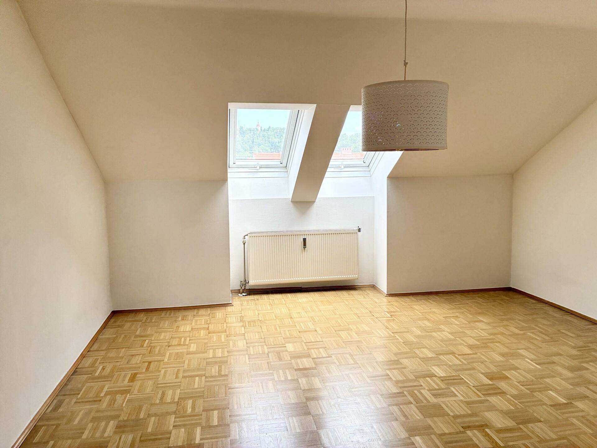 Helles Zimmer im Dachgeschoss mit Parkettboden, Dachschräge und Dachfenster.