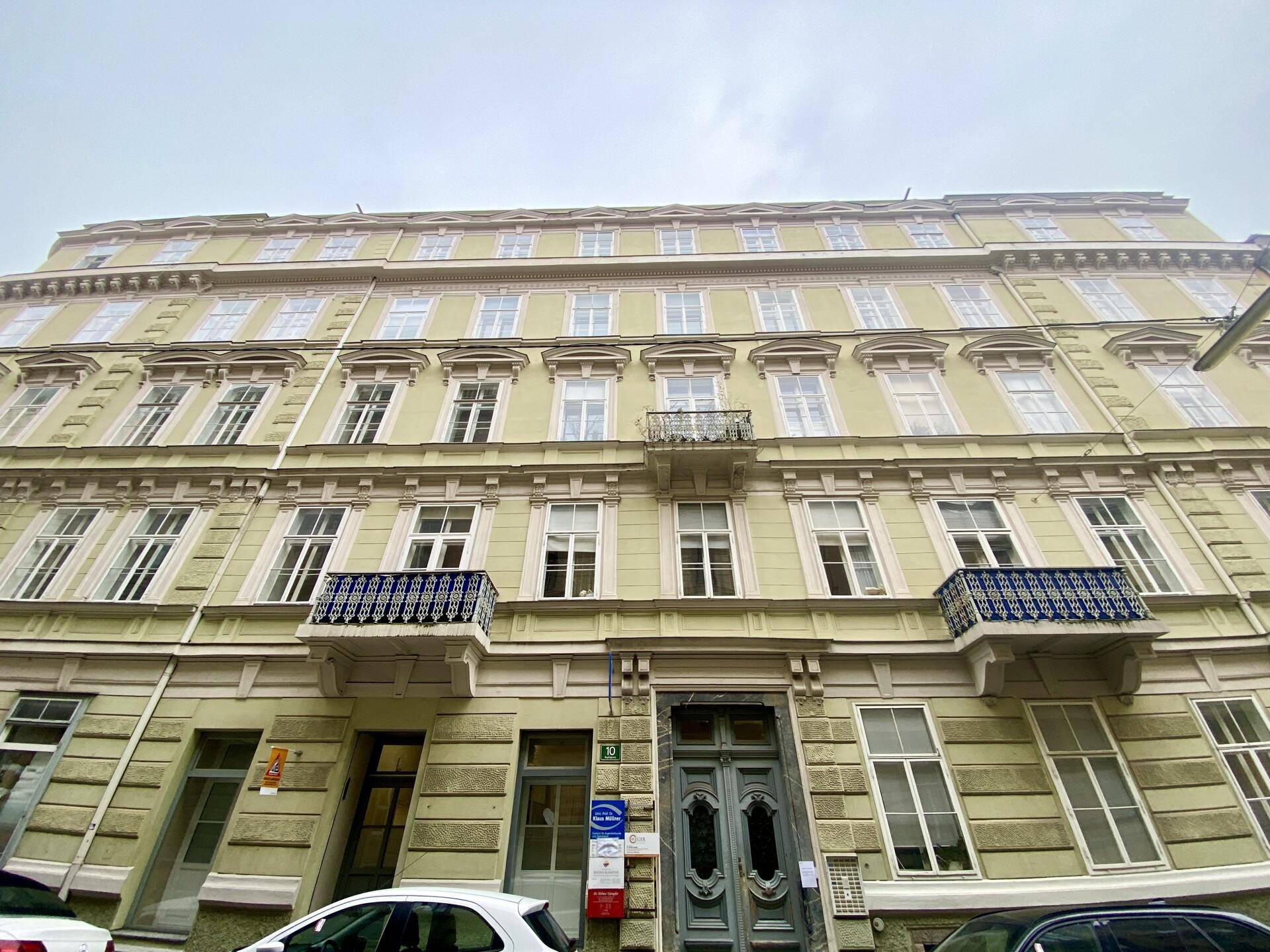 Historische Fassade eines Mehrfamilienhauses mit vielen Fenstern und kleinen Balkonen.