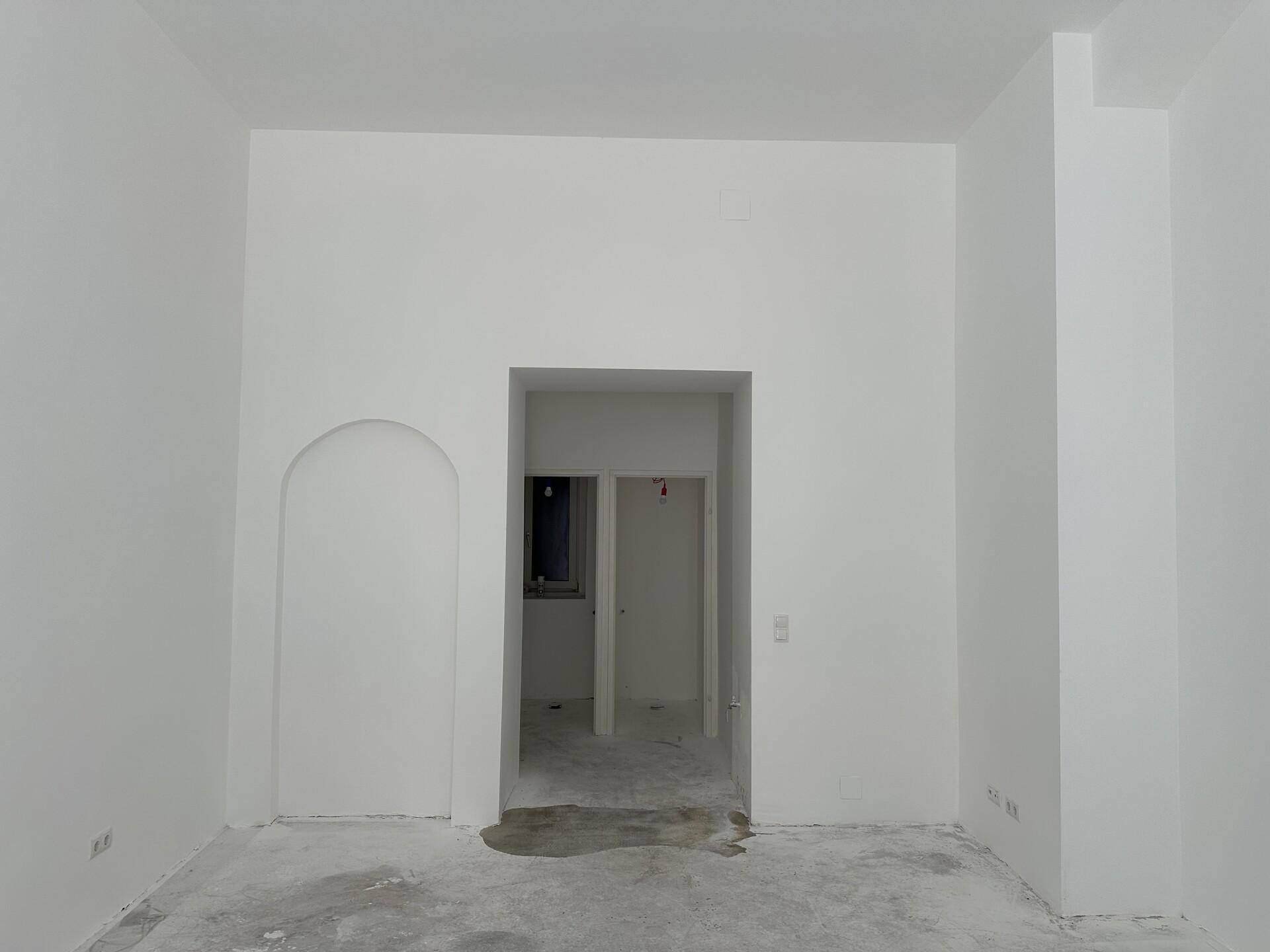 Leerer Raum mit frisch gestrichenen weißen Wänden und einem Betonboden, bereit für den Ausbau.