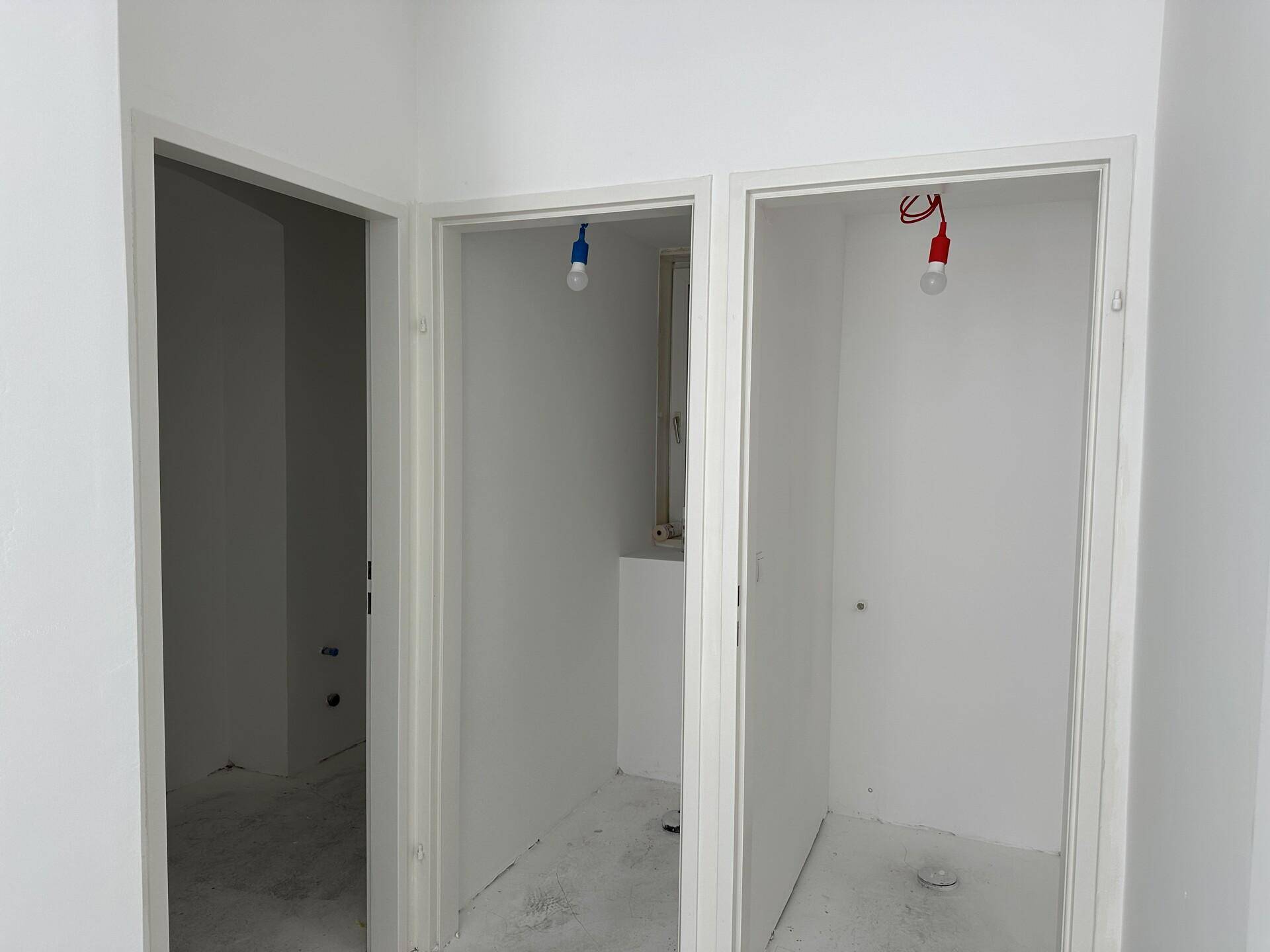 Zwei kleine, unfertige Räume mit weißen Wänden und sichtbaren Elektroinstallationen, möglicherweise für Sanitäranlagen.