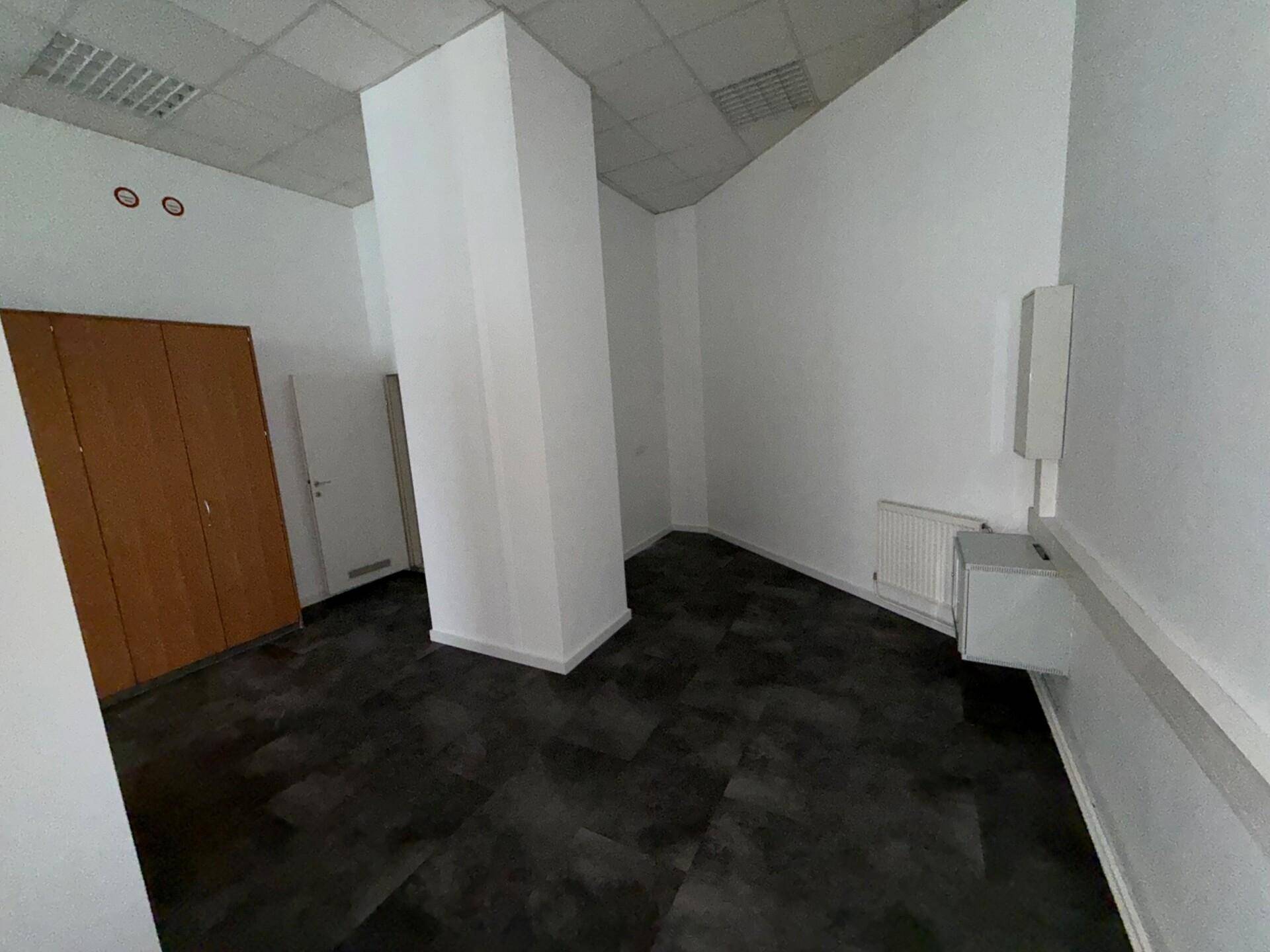 Eckbereich eines Büroraums mit dunklem Vinylboden, weißem Pfeiler und Heizkörper an der Wand.
