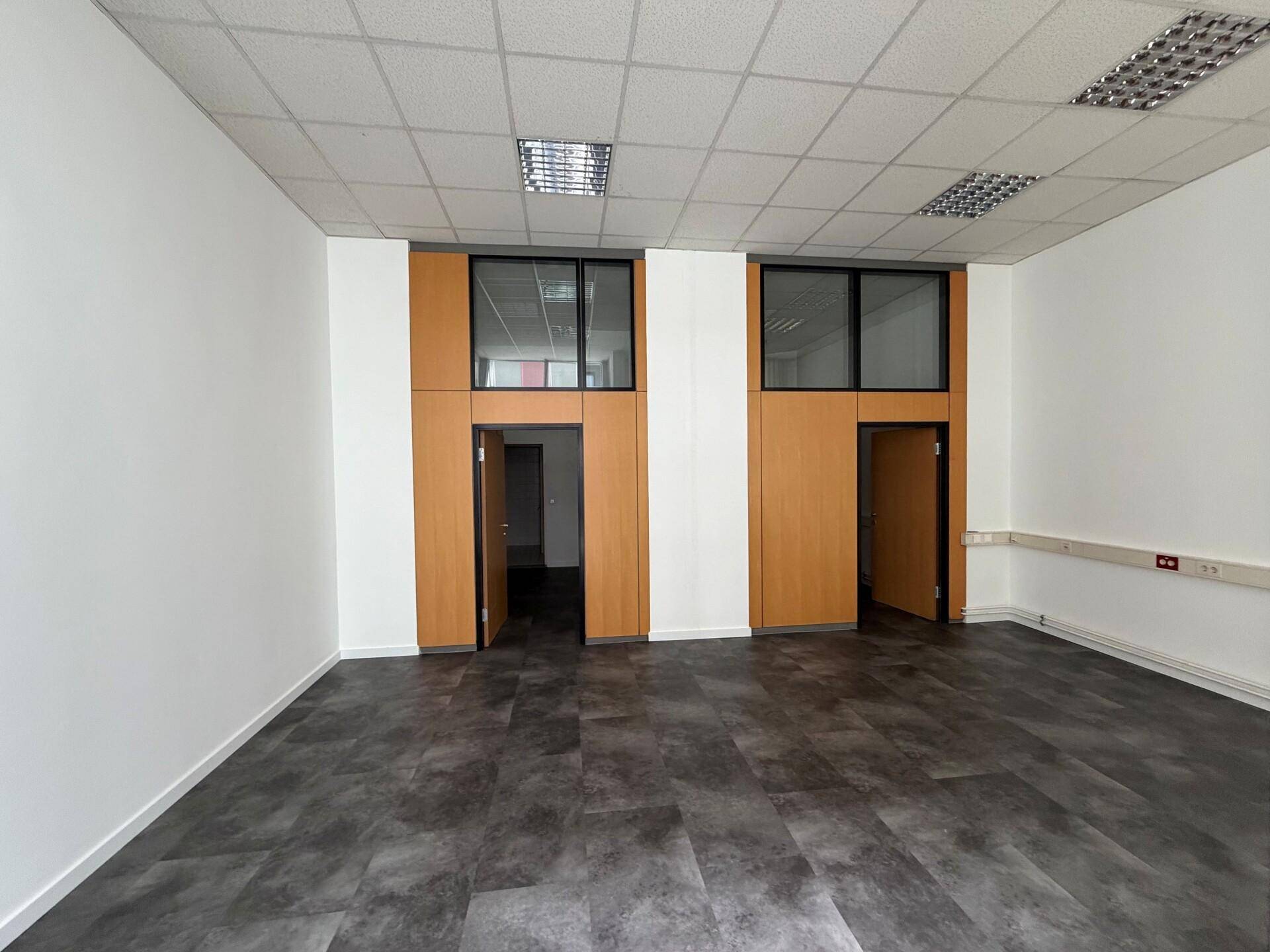 Leerer Büroraum mit dunklem Vinylboden, weißen Wänden und Holzpaneelen, bereit zur individuellen Gestaltung.