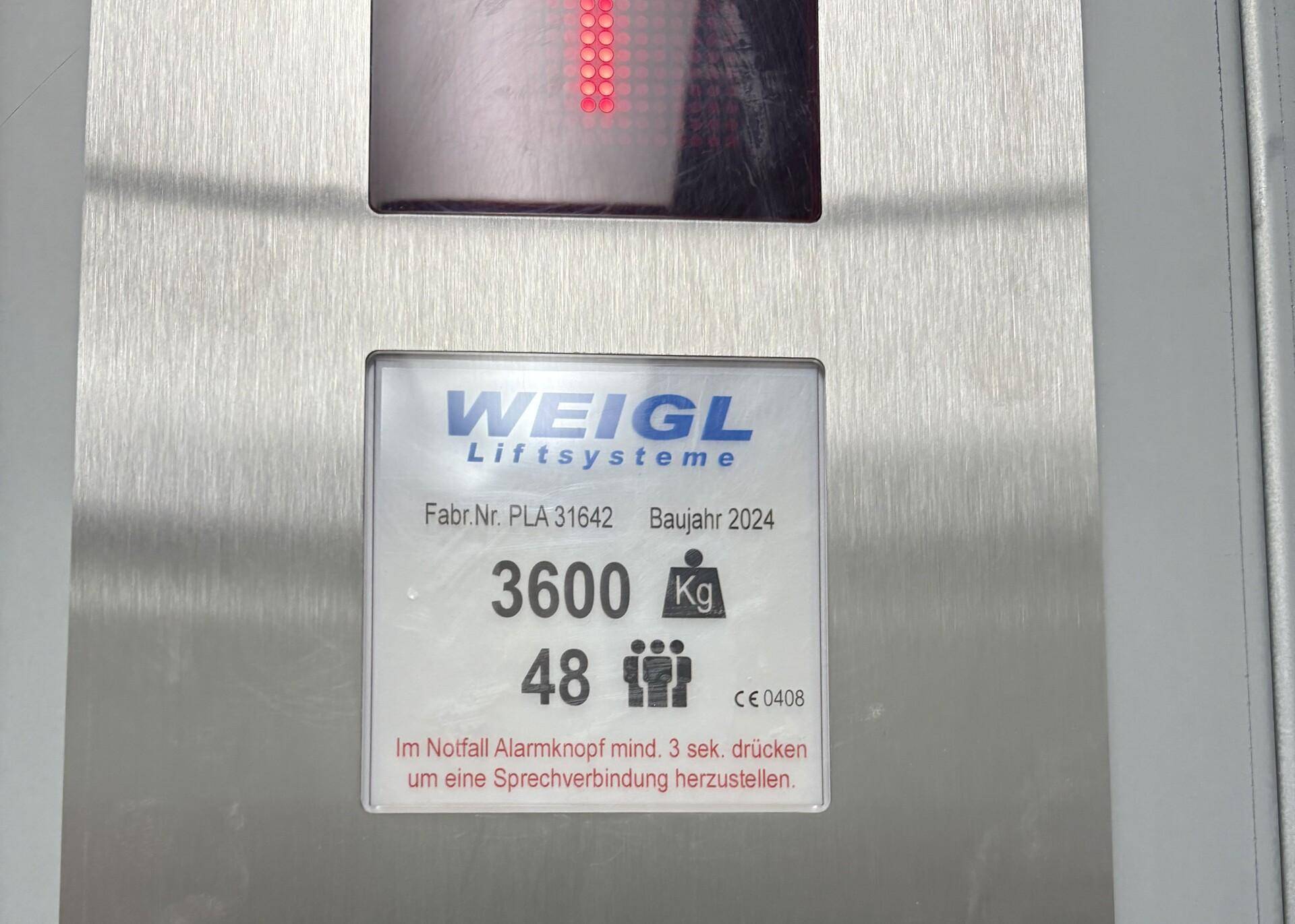 Nahaufnahme eines Aufzugspanels der Firma Weigl Liftsysteme mit Baujahr 2024 und Traglastangaben.